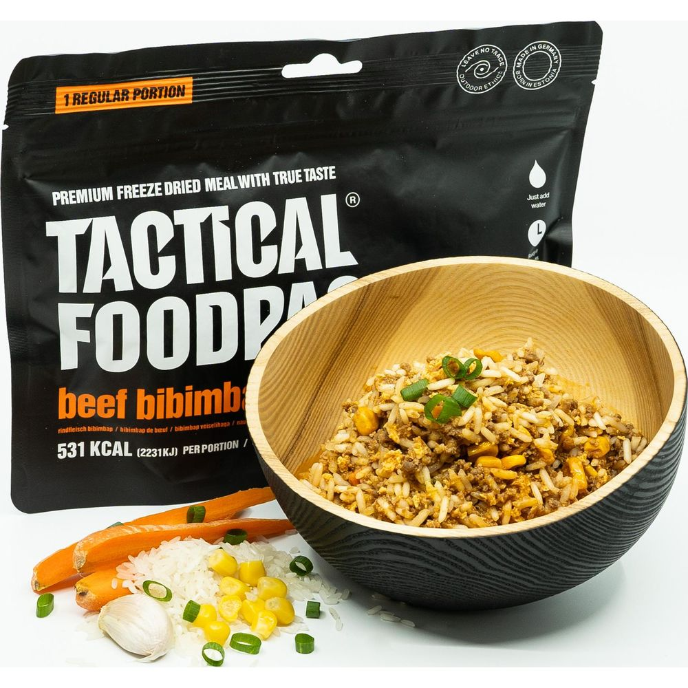 Una busta di Tactical Foodpack Beef Bibimbap accanto a una ciotola di legno con pasto pronto.