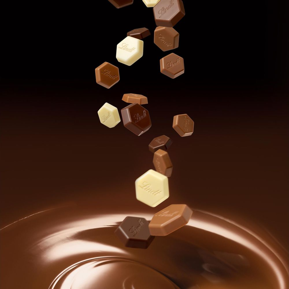 Cioccolatini Lindt assortiti cadono nel cioccolato fuso su sfondo marrone scuro.