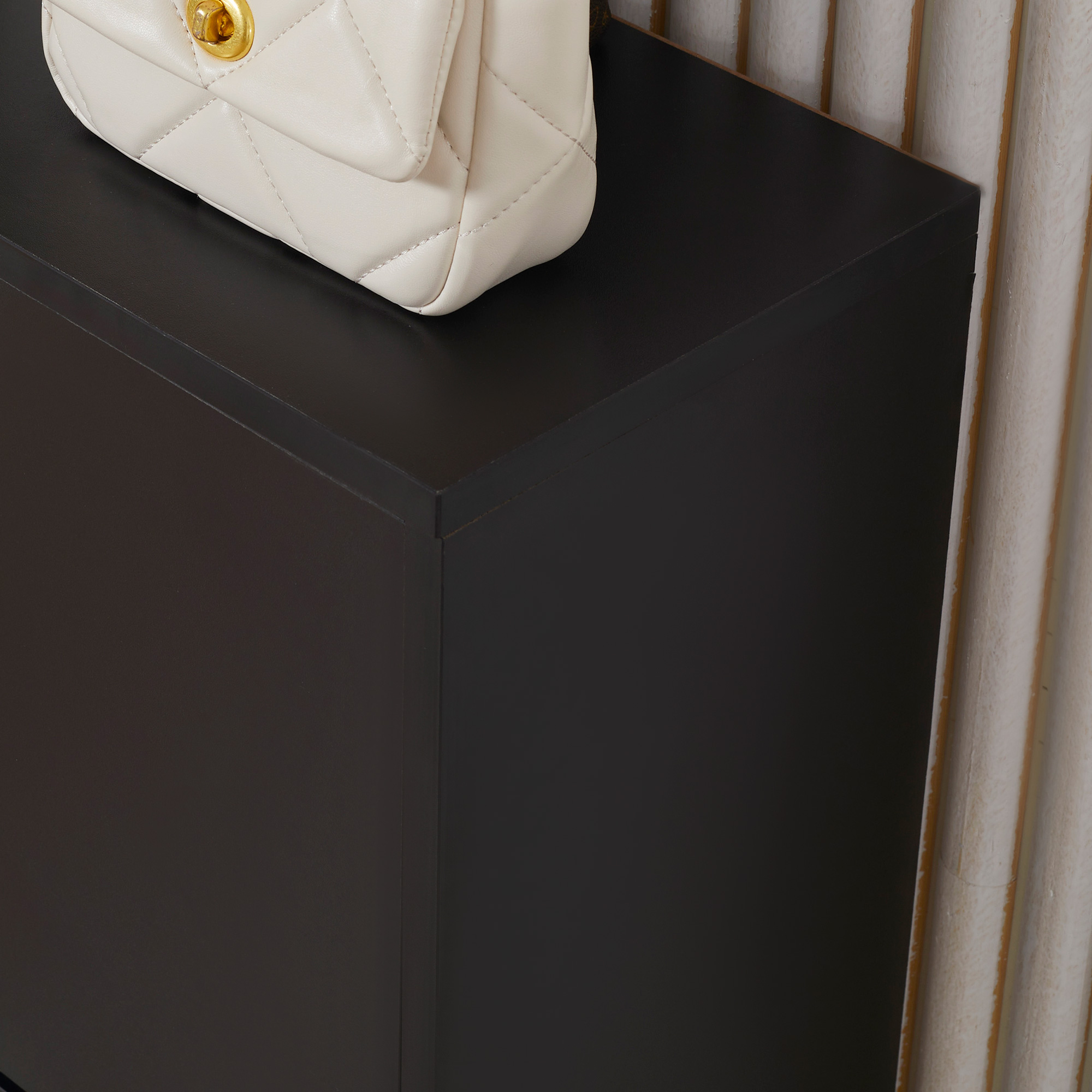 Un bolso acolchado color crema con cierre dorado descansa sobre un estante negro.