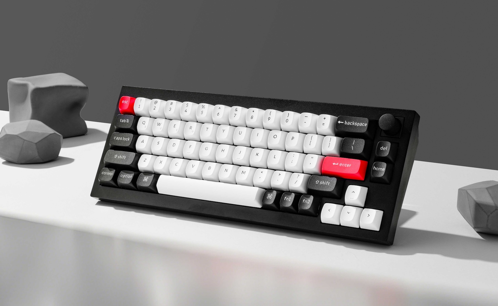 Czarna klawiatura z białymi klawiszami i czerwonymi akcentami, obok szarych obiektów.