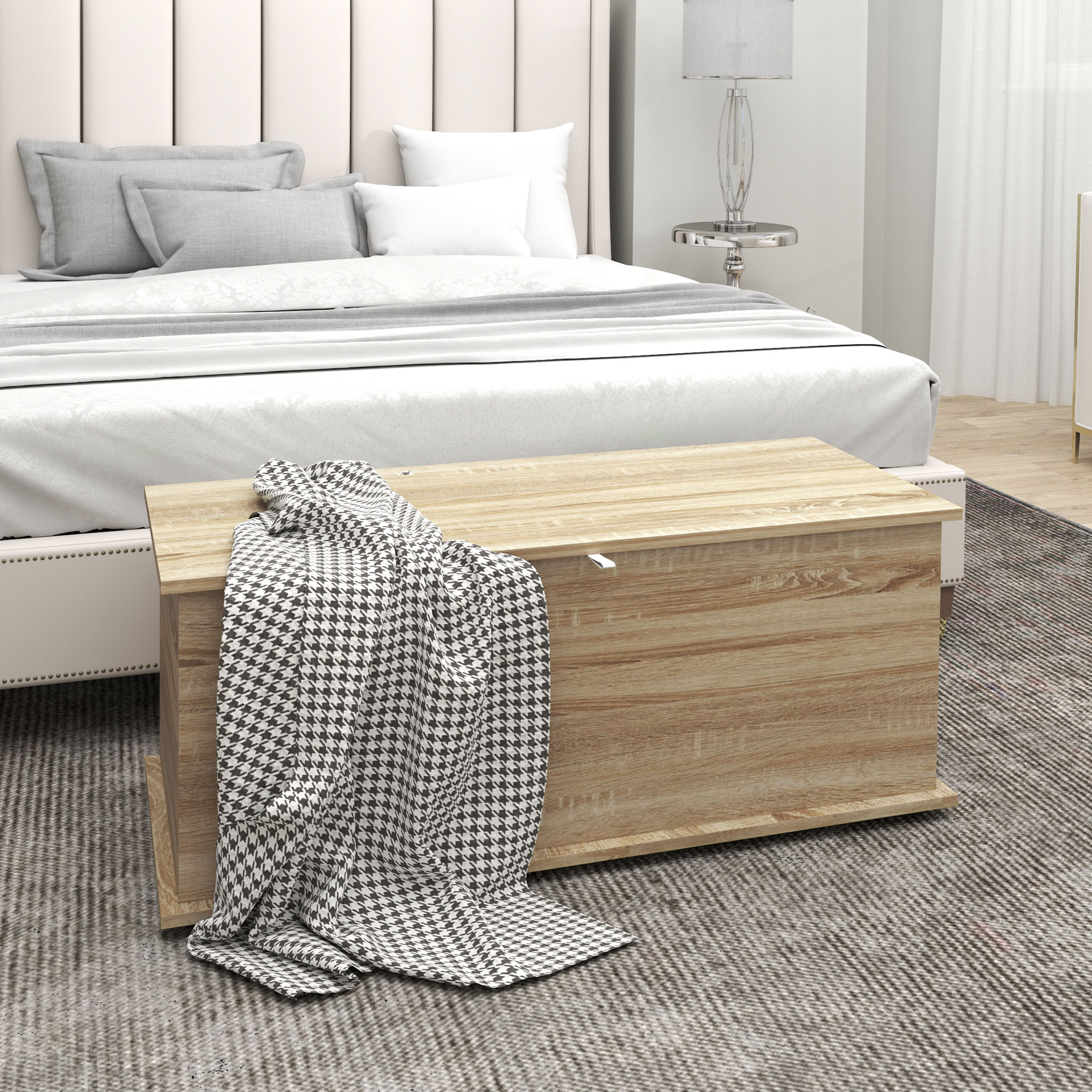 Un baúl de almacenamiento de madera se sienta frente a una cama con almohadas.