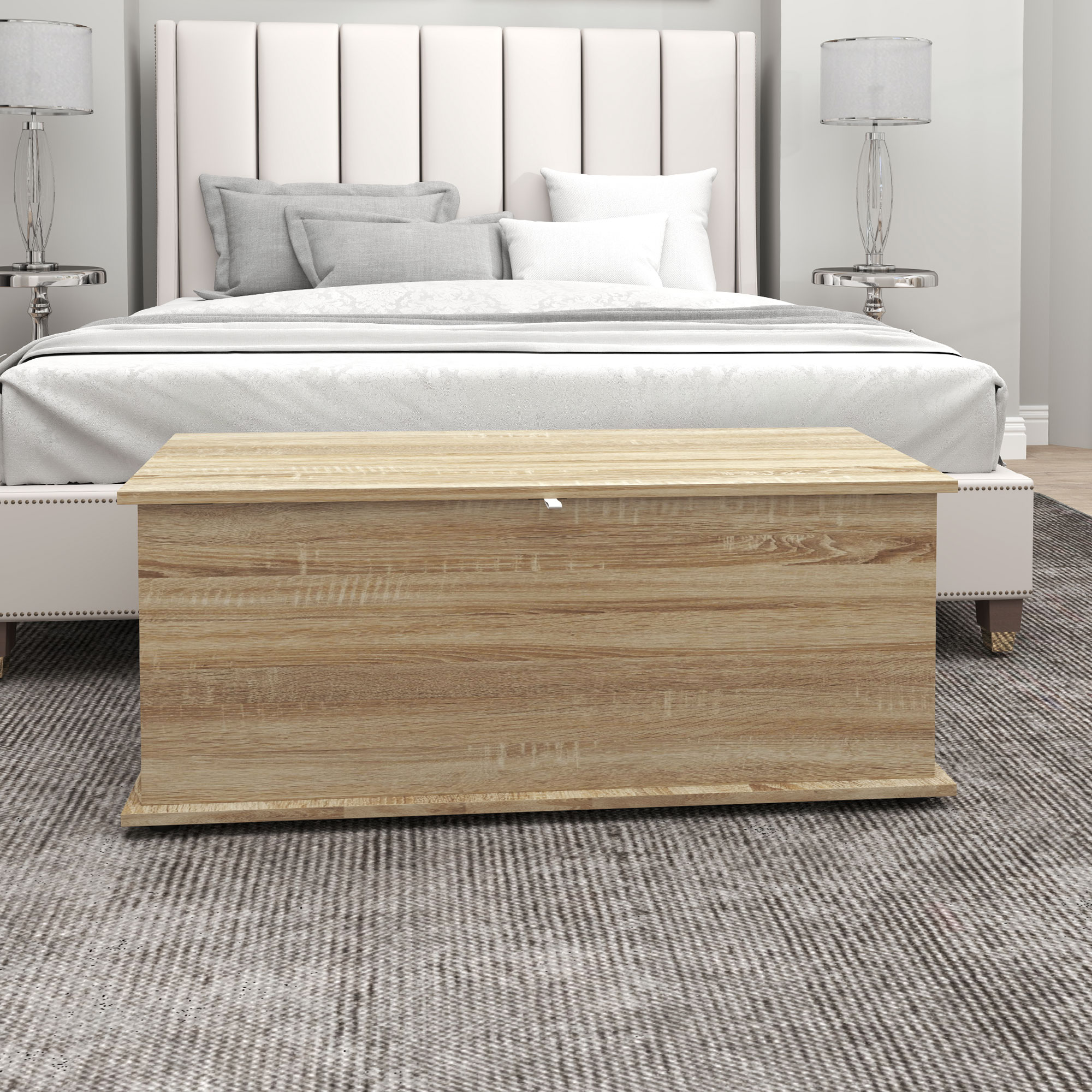 Un baúl de madera clara frente a una cama con cabecero blanco.