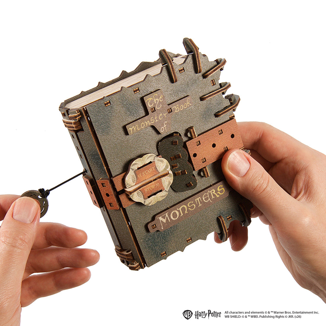 Hände halten das "Monsterbuch der Monster", ein Holzmodell mit Schnur und Anhänger.