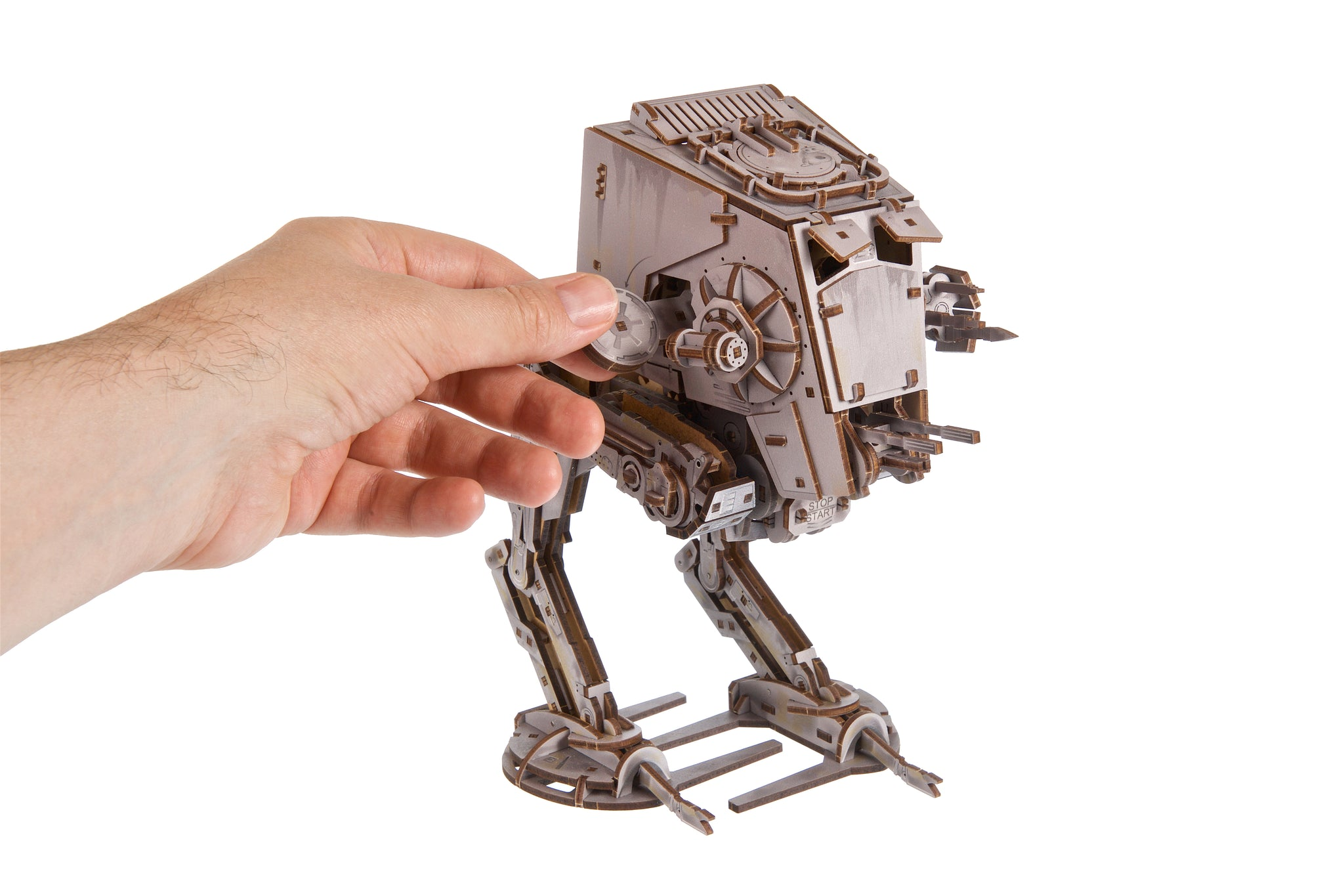 Eine Hand hält ein hölzernes Modell eines AT-ST-Walkers auf weißem Hintergrund.