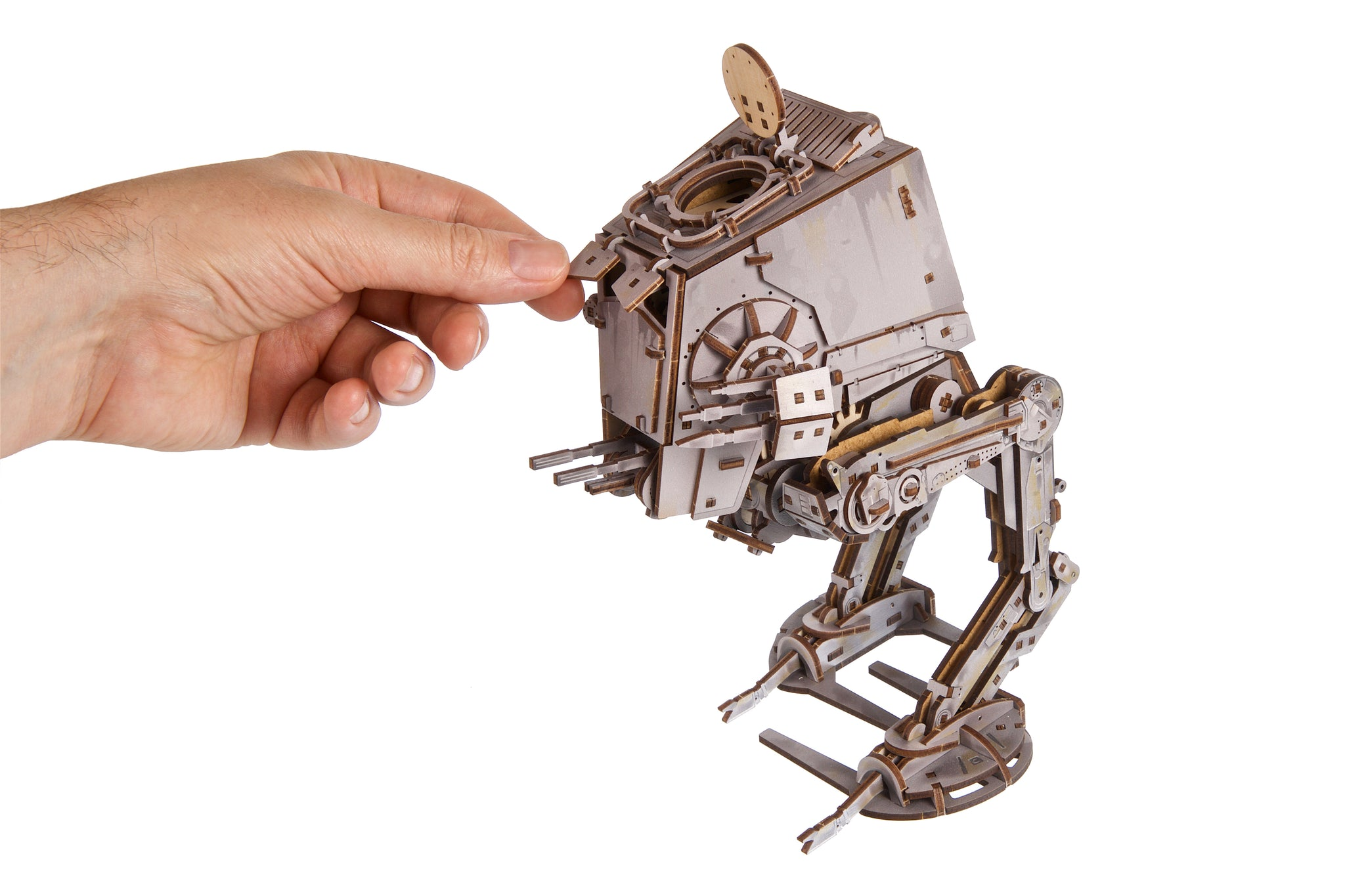 Eine Hand berührt ein hölzernes Modell eines AT-ST-Läufers auf weißem Hintergrund.
