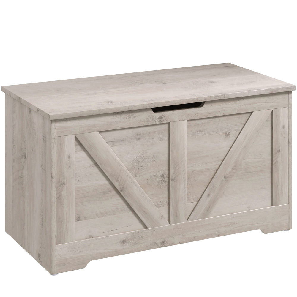Un baúl de madera clara con panel frontal estilo puerta de granero y asa negra.