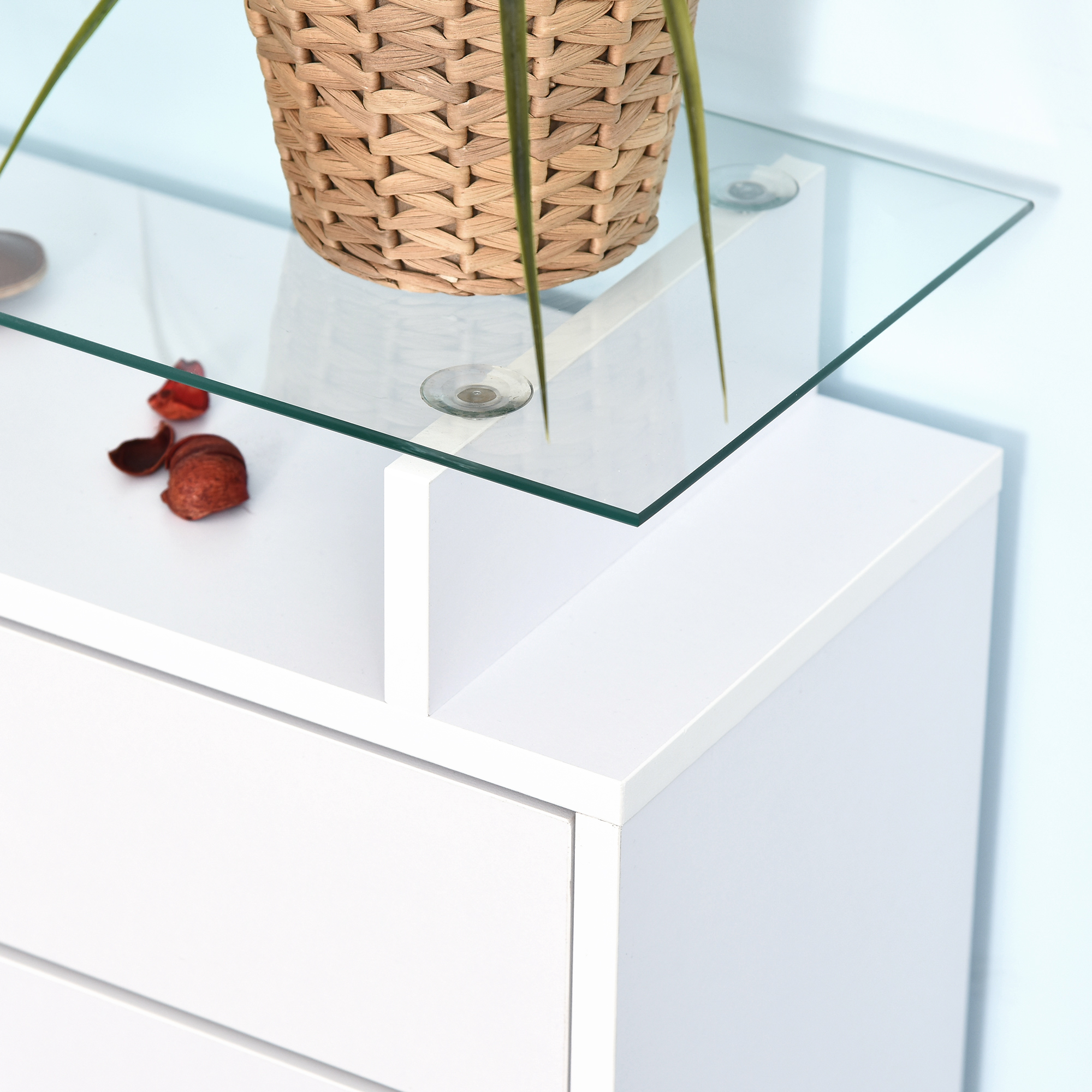 Mueble blanco con tapa de cristal, cesta tejida y pétalos decorativos.