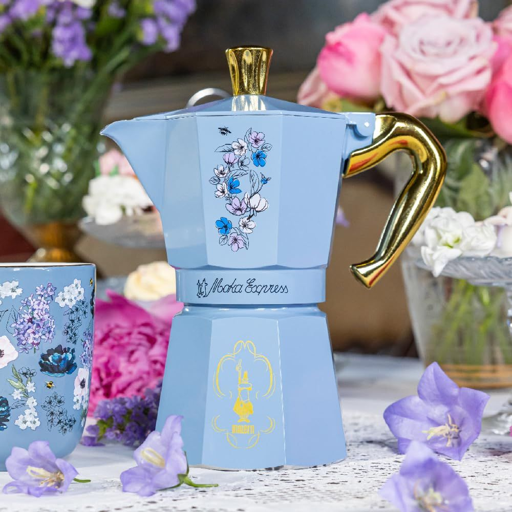 Moka Express azzurra con decoro floreale e manico dorato.