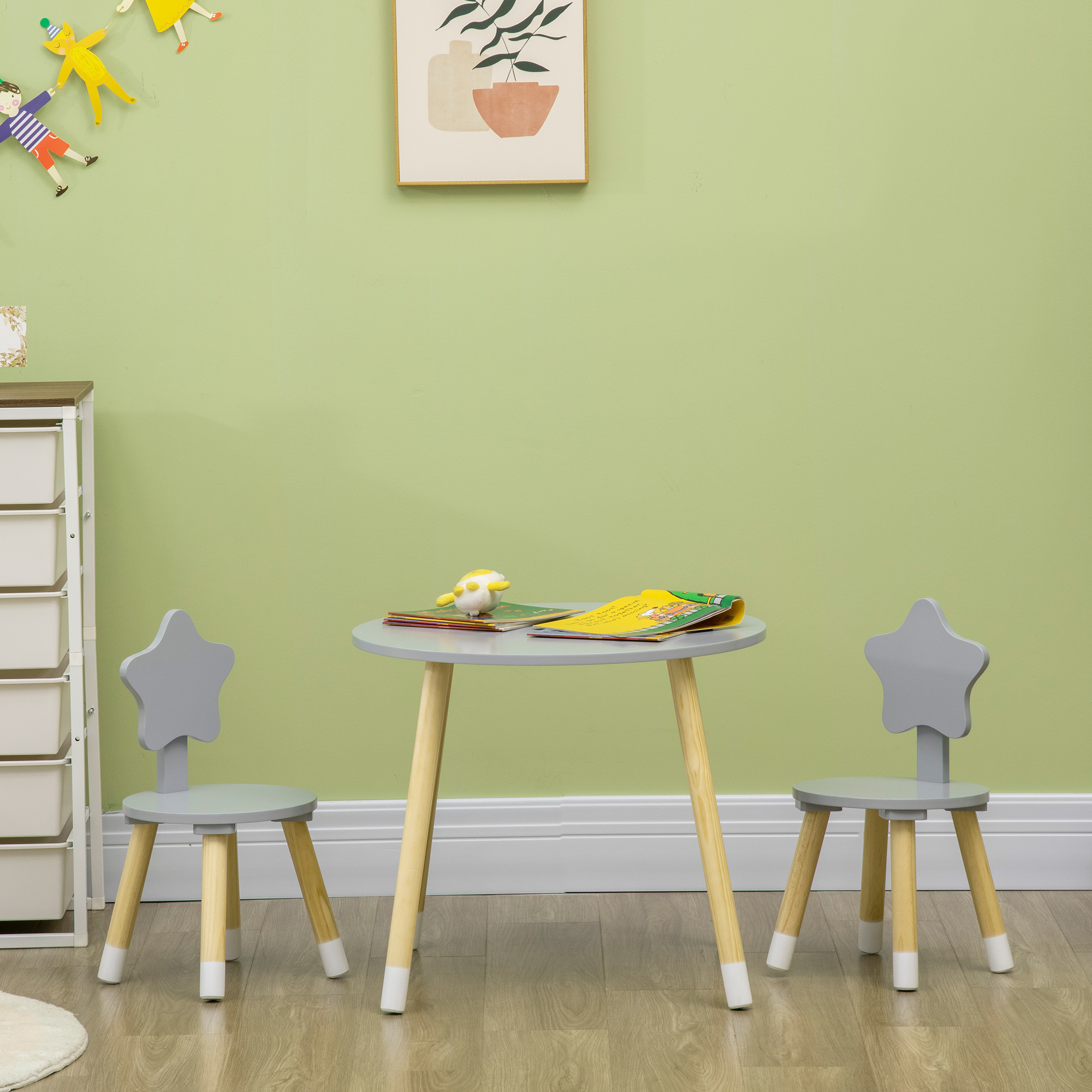 Una mesa infantil gris con sillas de respaldo estrellado y libros. Estante blanco a la izquierda.