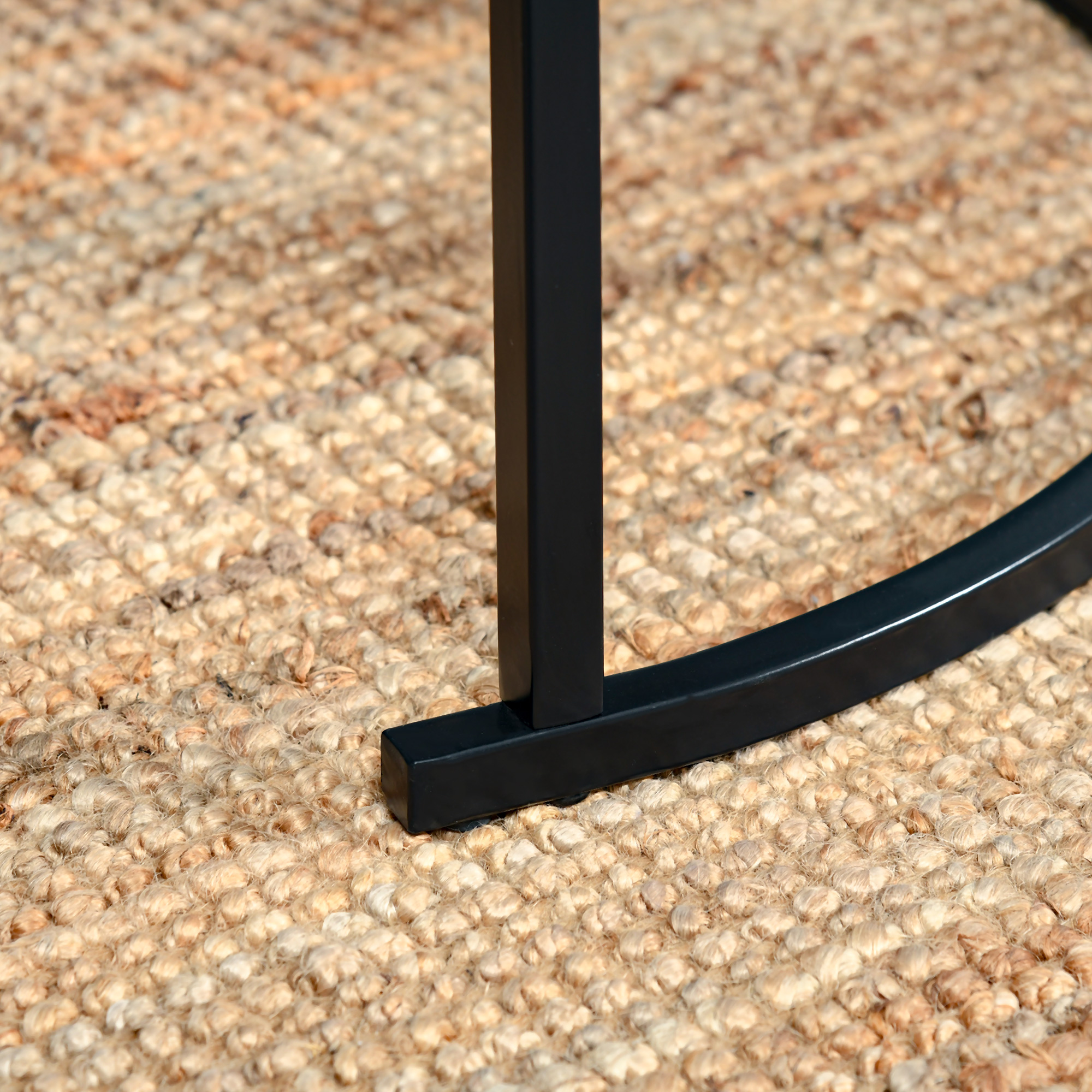 Una pata de mueble de metal negro descansa sobre una alfombra tejida texturizada beige.