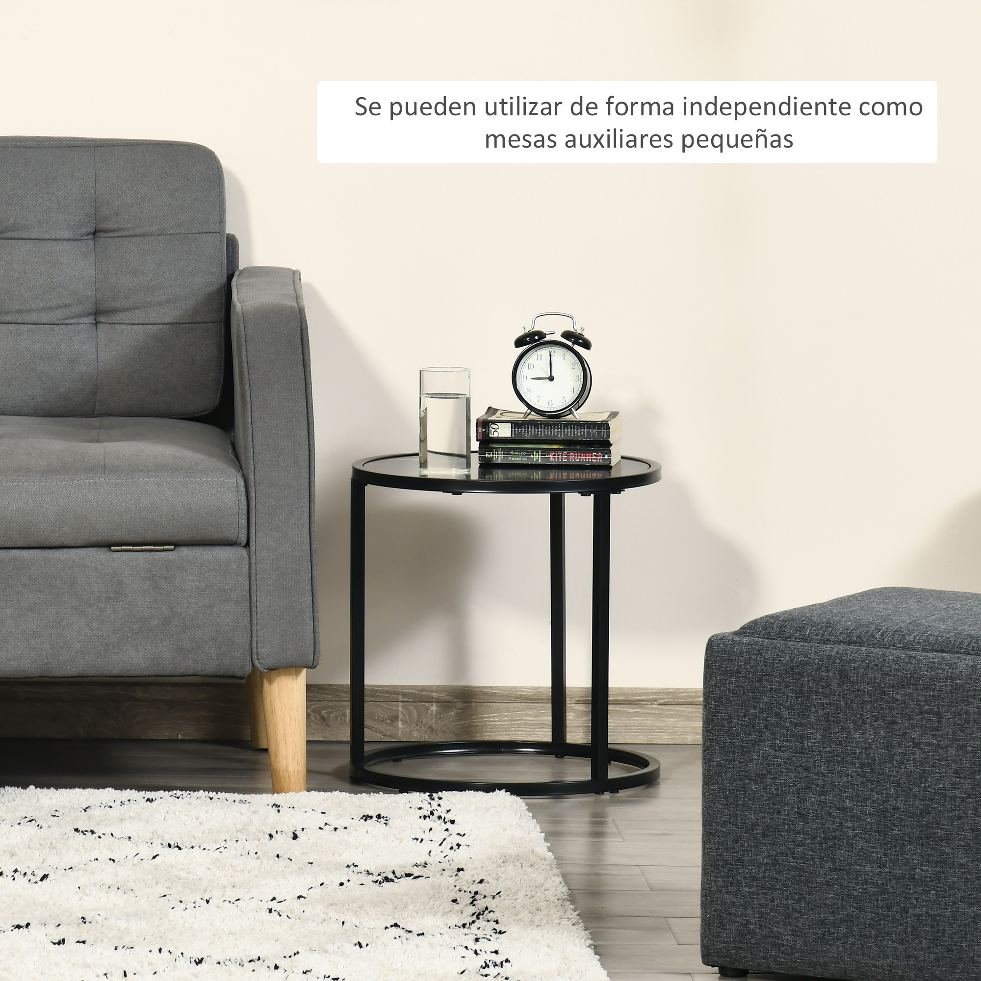 Un sillón gris, una mesa auxiliar redonda con libros, un vaso y un despertador.