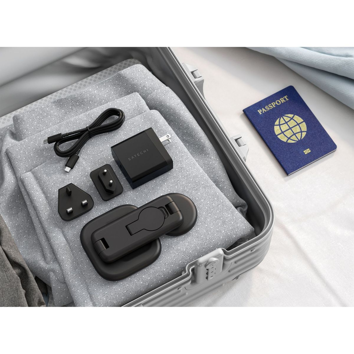 Ein schwarzer Reiseadapter, Kabel und ein Reisepass liegen in einem offenen Koffer.