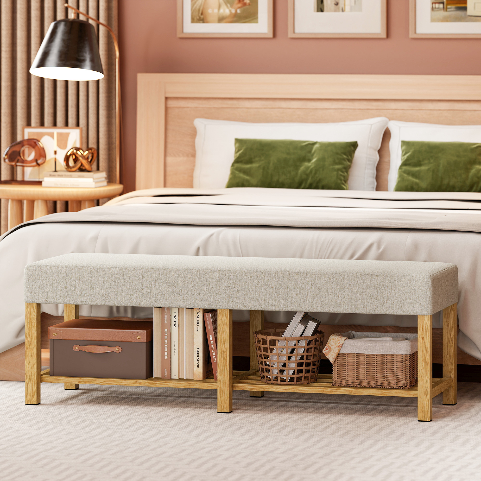 Un banco beige con marco de madera está frente a una cama. Debajo hay libros, una caja marrón y una cesta.