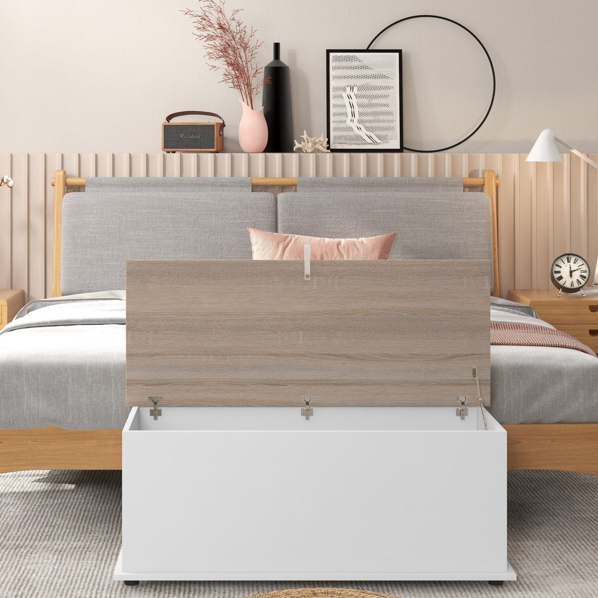 Cama abierta con tapa de madera, baúl blanco, mesita de noche, lámpara y decoración.