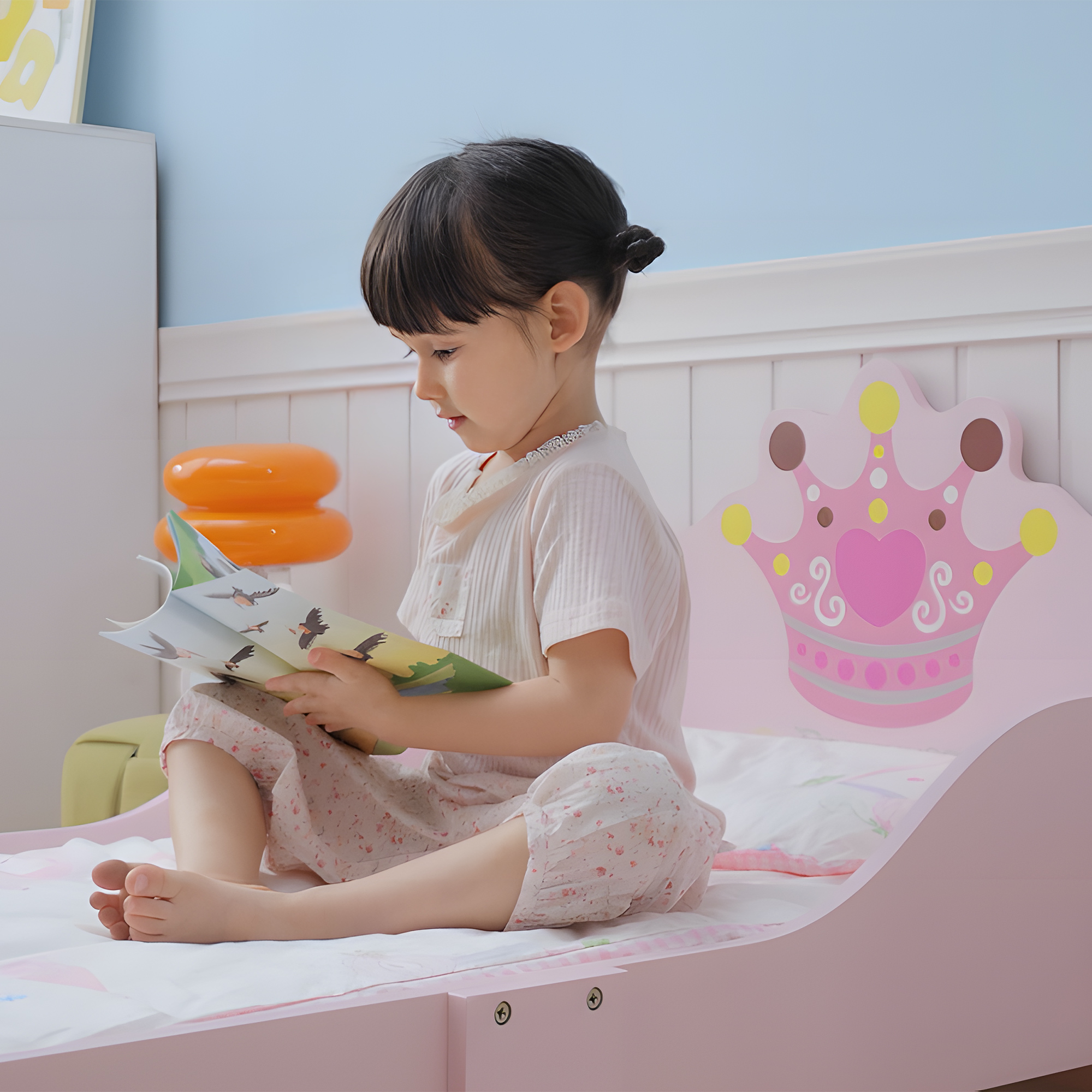 Una niña lee un libro con dibujos de pájaros en una cama rosa con decoración de corona.