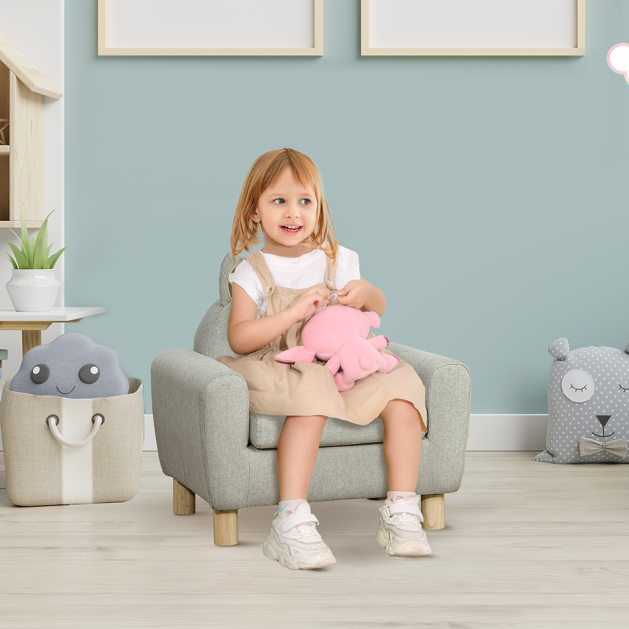 Una niña de pelo rubio se sienta en un sillón sosteniendo un peluche rosa.
