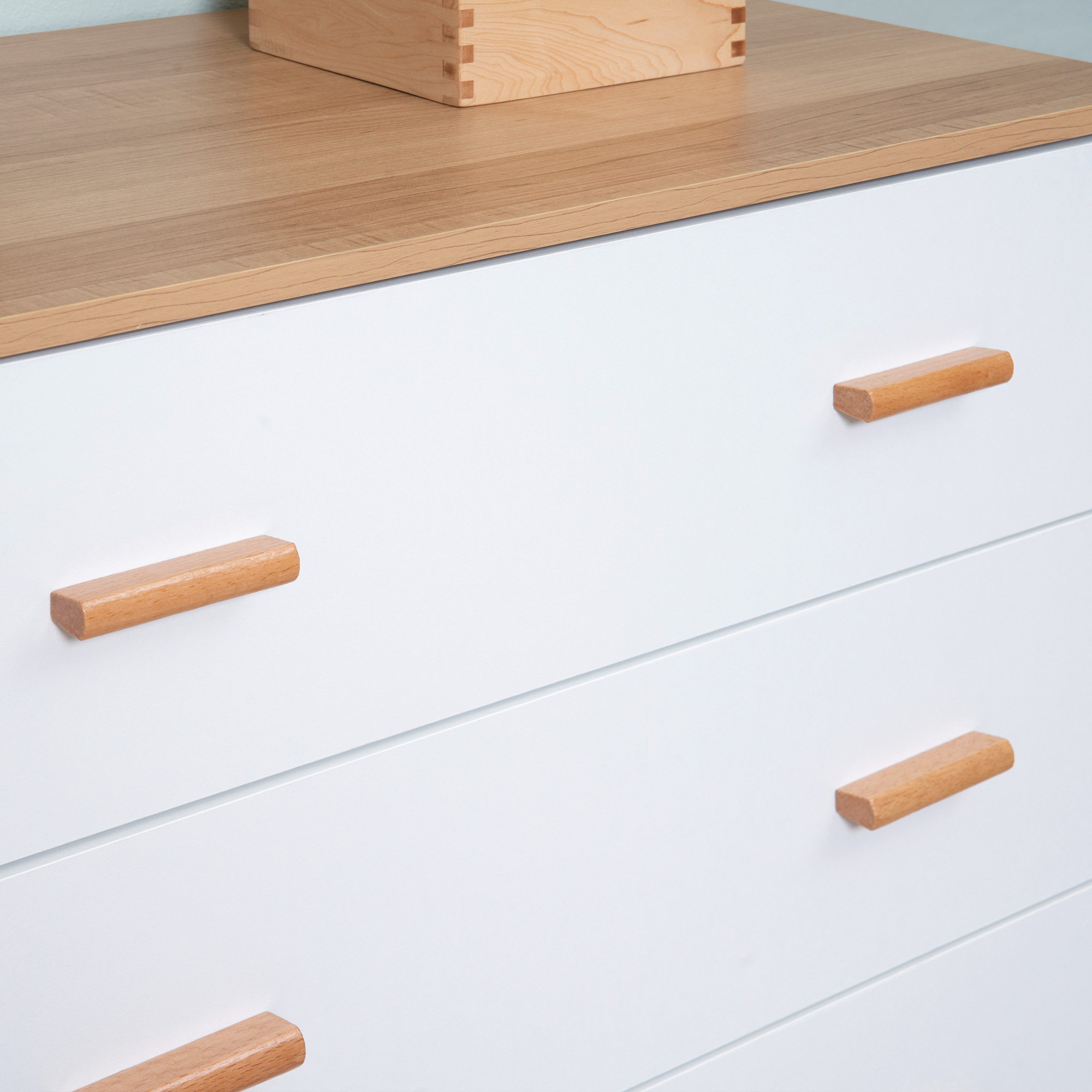 Cómoda blanca con cajones de tirador de madera y una caja de madera encima.
