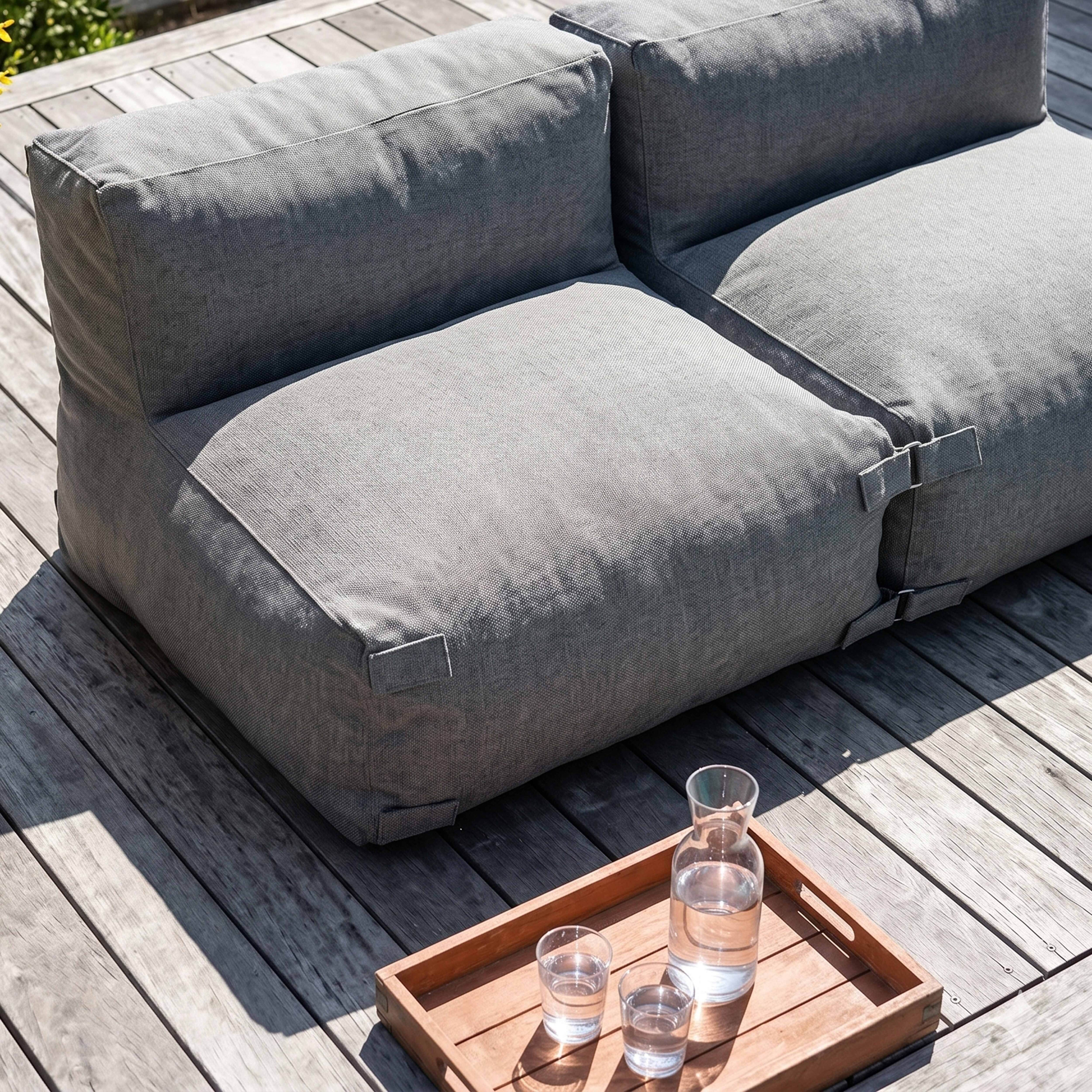 Graues Outdoor-Sofa auf Holzdeck mit Holzlöffel und Gläsern.