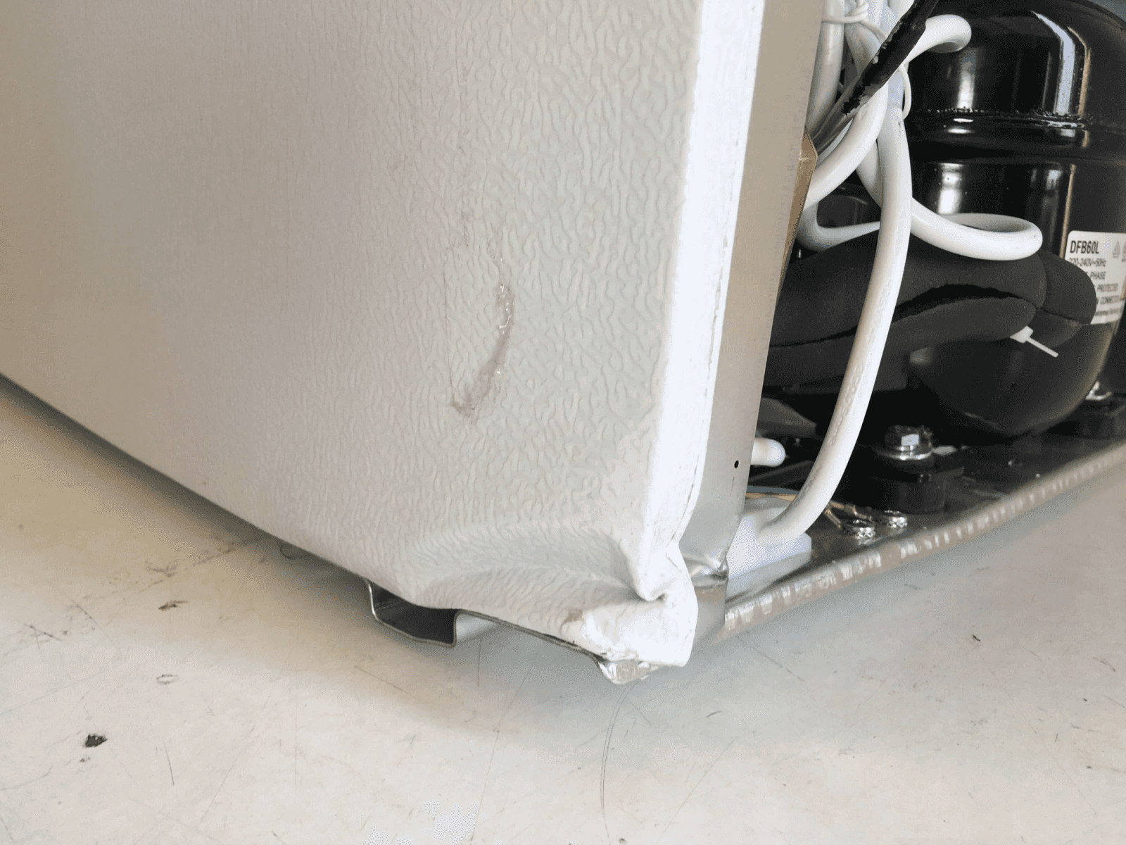Lato danneggiato del frigorifero bianco con compressore e fili.