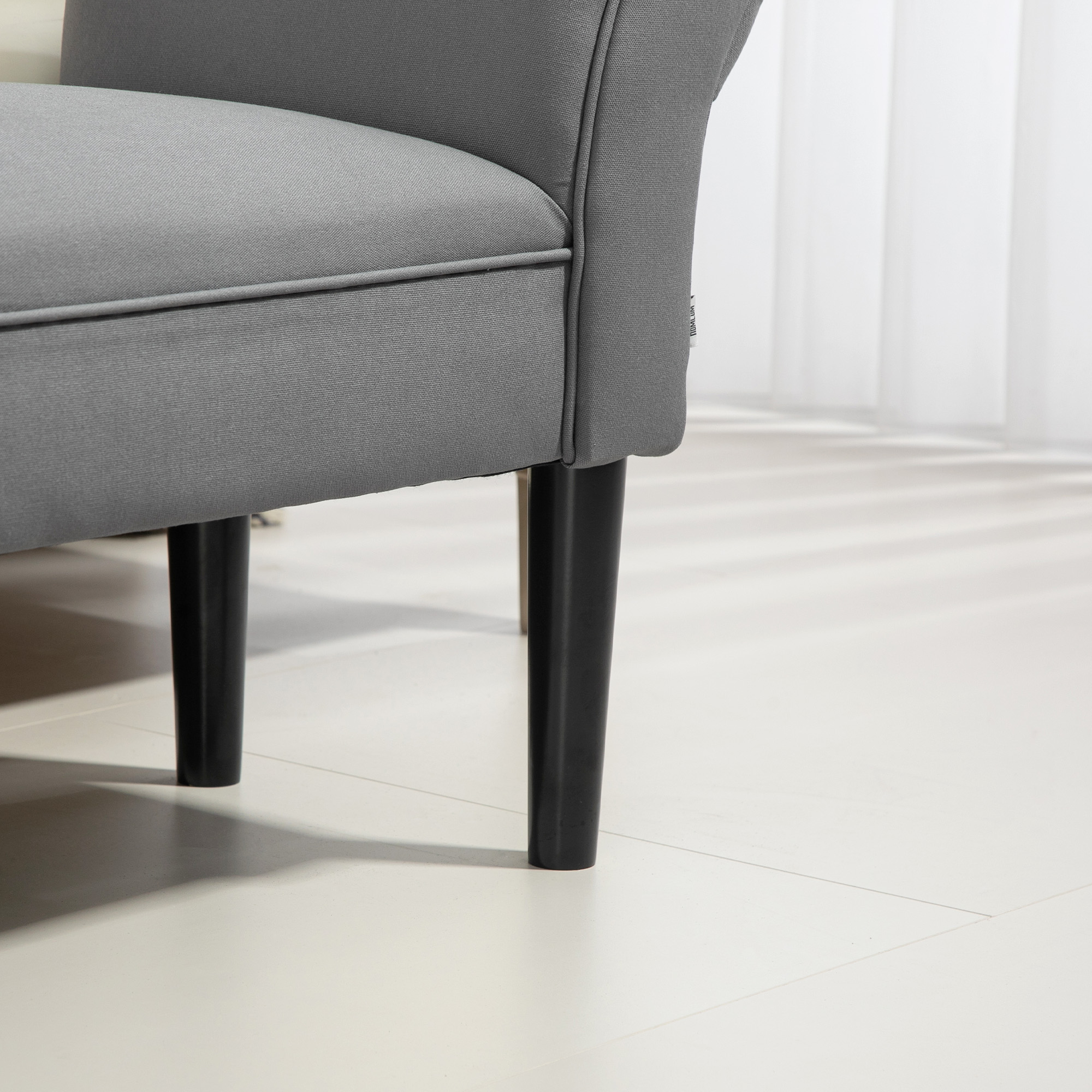 Primer plano de un sillón tapizado gris con patas oscuras sobre suelo blanco.