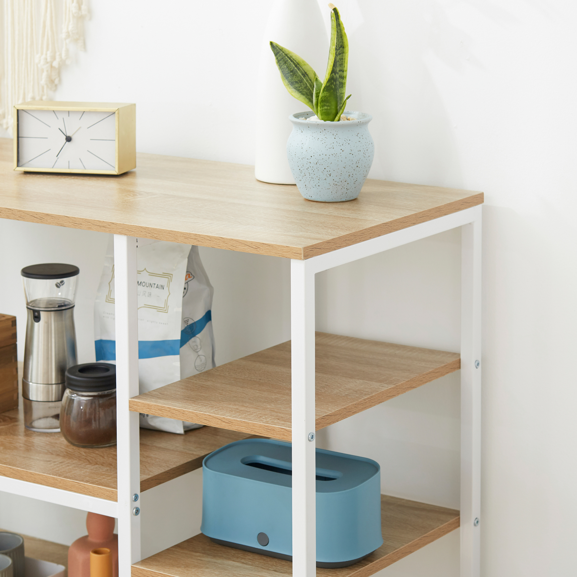 Un estante de madera con reloj, planta, molinillo de café, frascos, bolsas y caja de pañuelos.