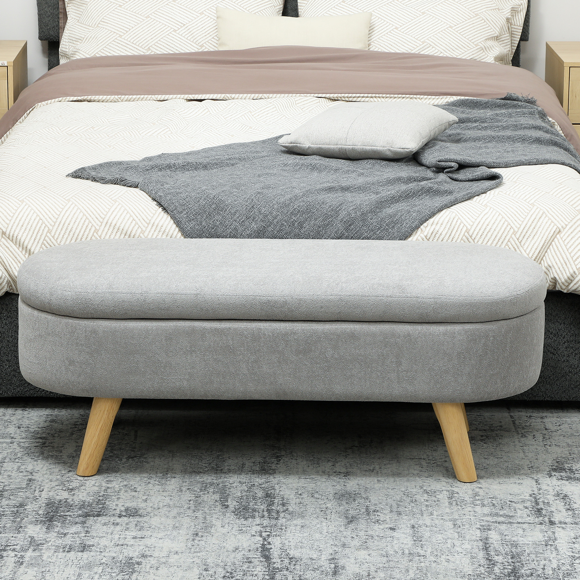 Banco de almacenamiento gris frente a una cama con mantas y cojines estampados.