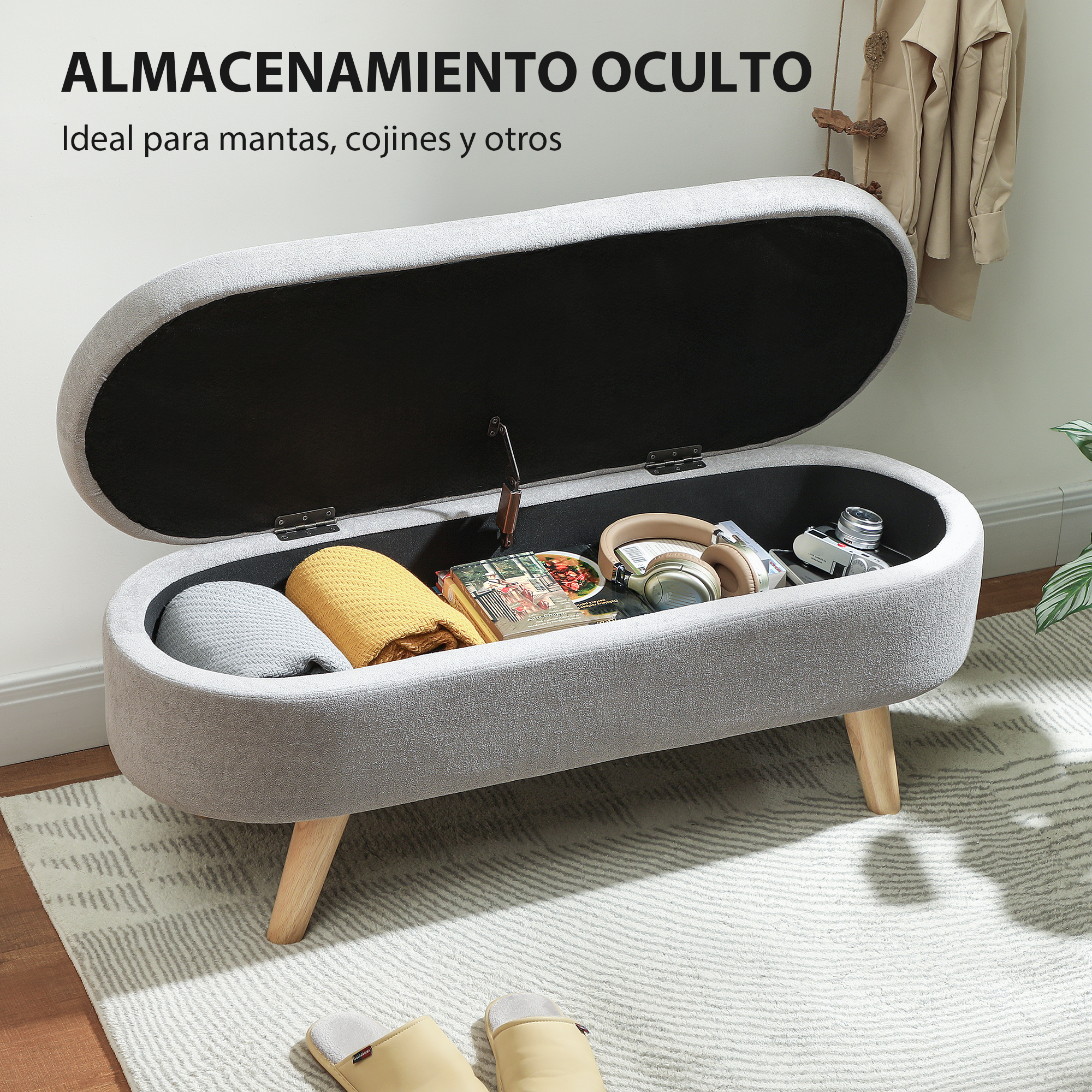 Banqueta de almacenamiento gris con tapa abierta, contiene mantas, audífonos, cámara.