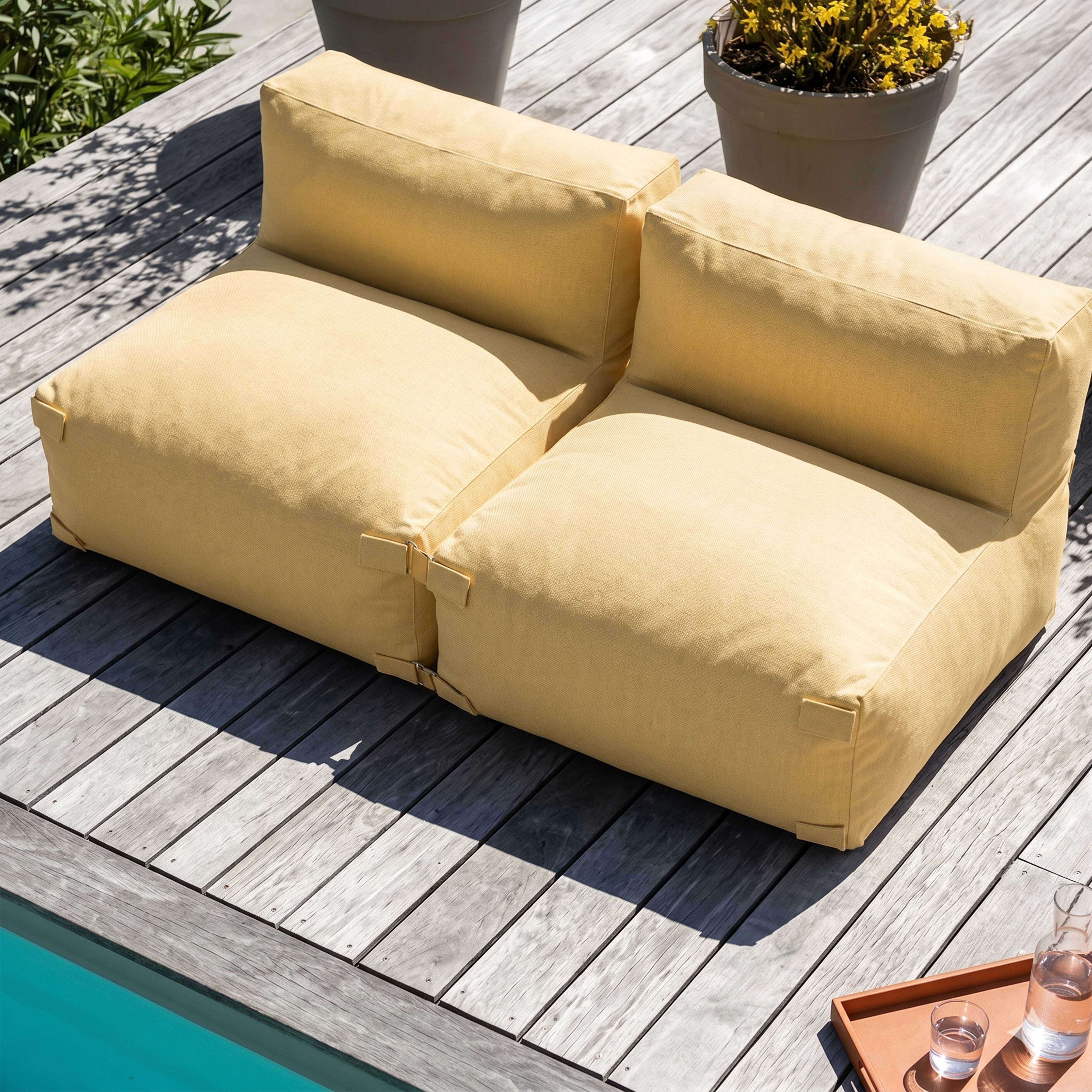 Ein gelbes Lounge-Möbel auf einer Holzterrasse neben einem Pool.