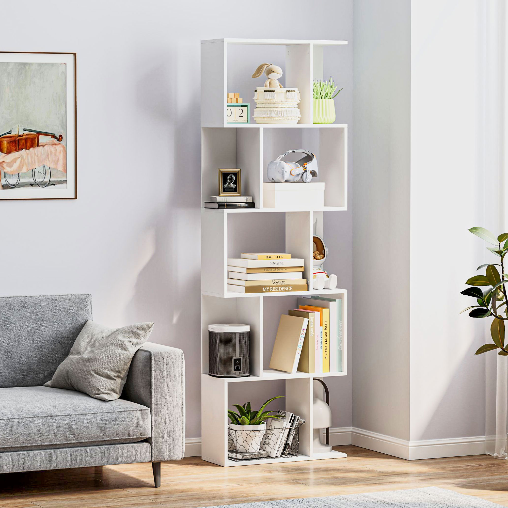 Una estantería blanca con decoración, libros y una planta junto a un sofá gris.