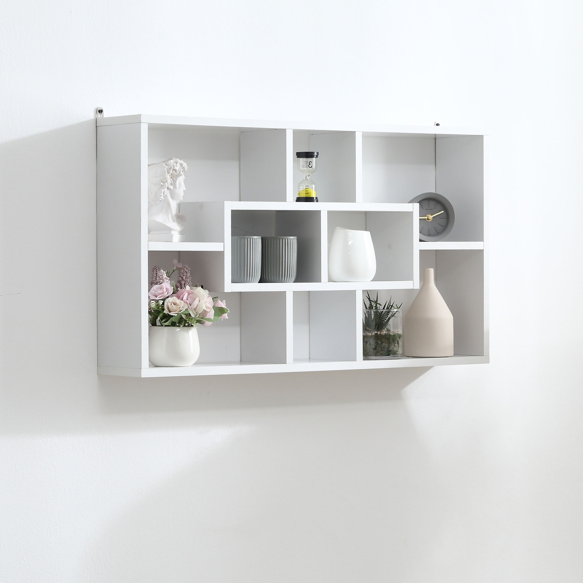 Un estante blanco con artículos decorativos: busto, reloj de arena, jarrones, plantas, reloj.