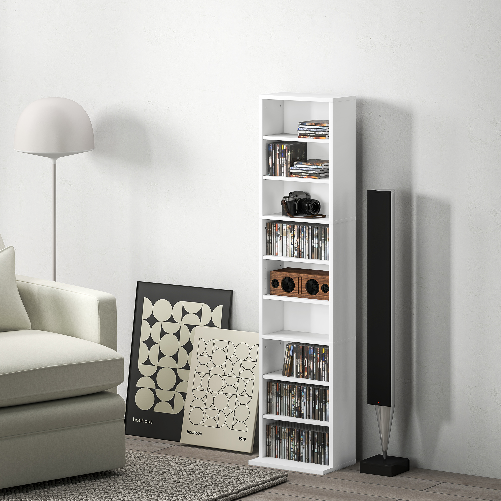 Una estantería blanca con CDs, una cámara y una radio de madera. Un sofá al lado.