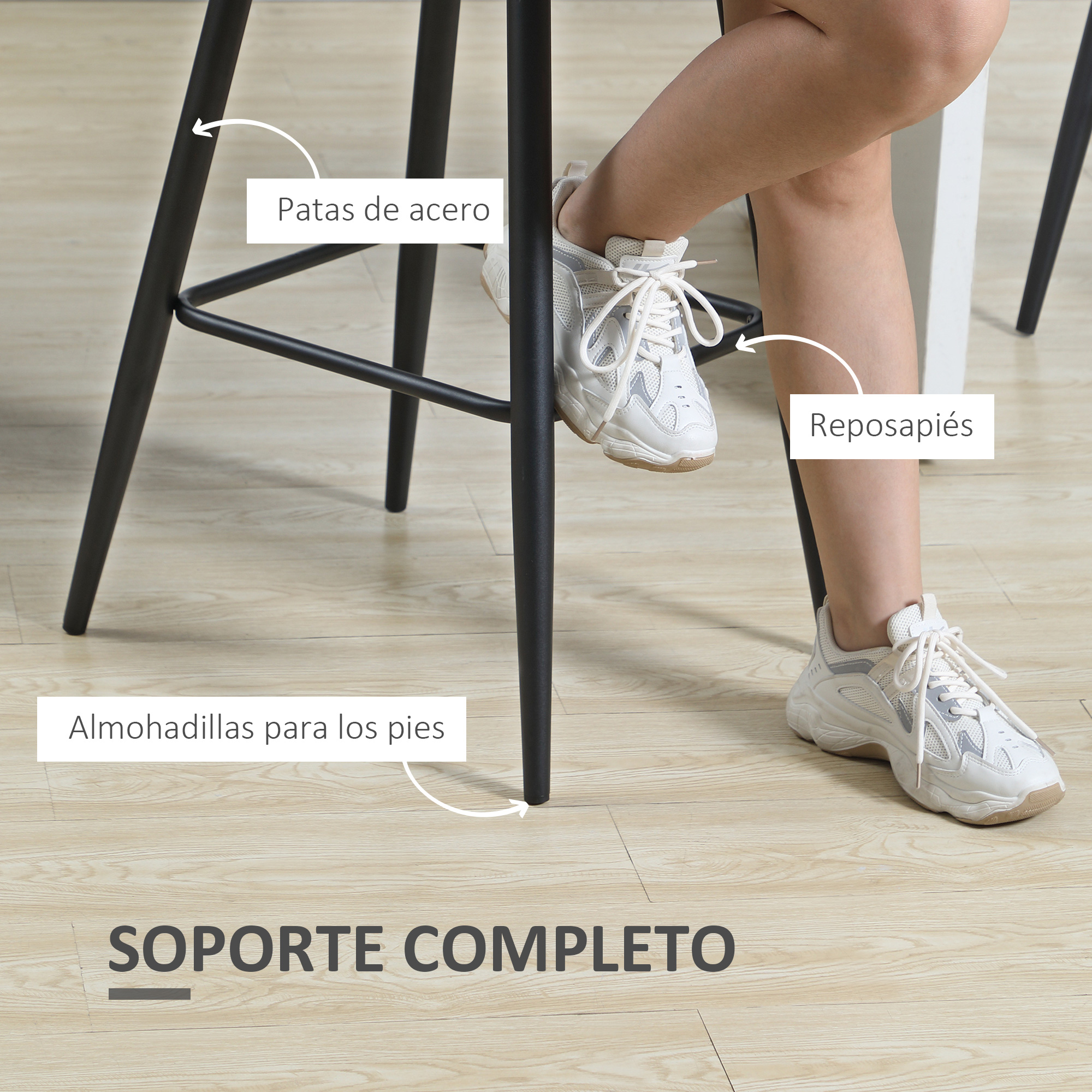 Primer plano de patas de taburete negras con pies en zapatillas blancas sobre suelo de madera.