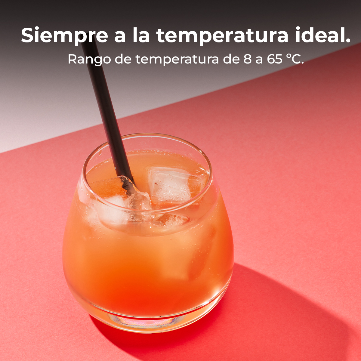 Un vaso con una bebida naranja y cubitos de hielo sobre una superficie roja.