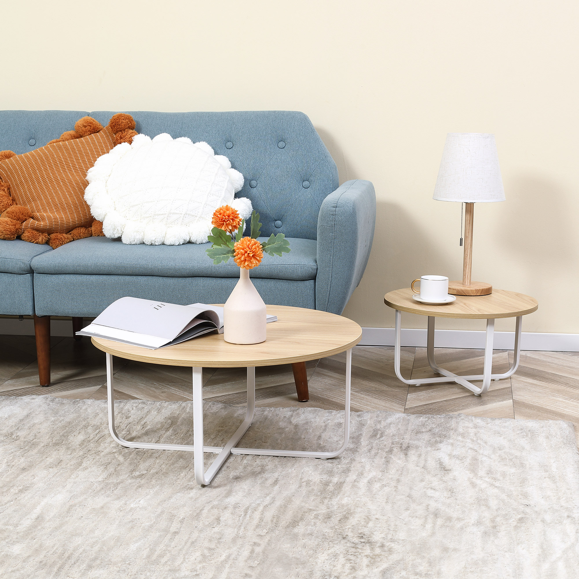 Sofá azul con cojines naranjas y blancos, mesa de centro redonda con jarrón, libro y mesa auxiliar con lámpara.
