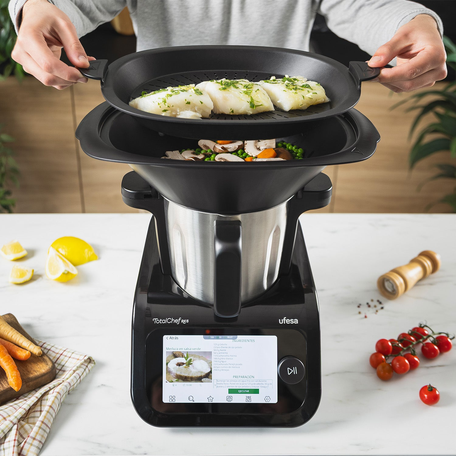 Una persona cocina al vapor pescado y verduras en una multi-olla, con limón, zanahorias y tomates cerca.