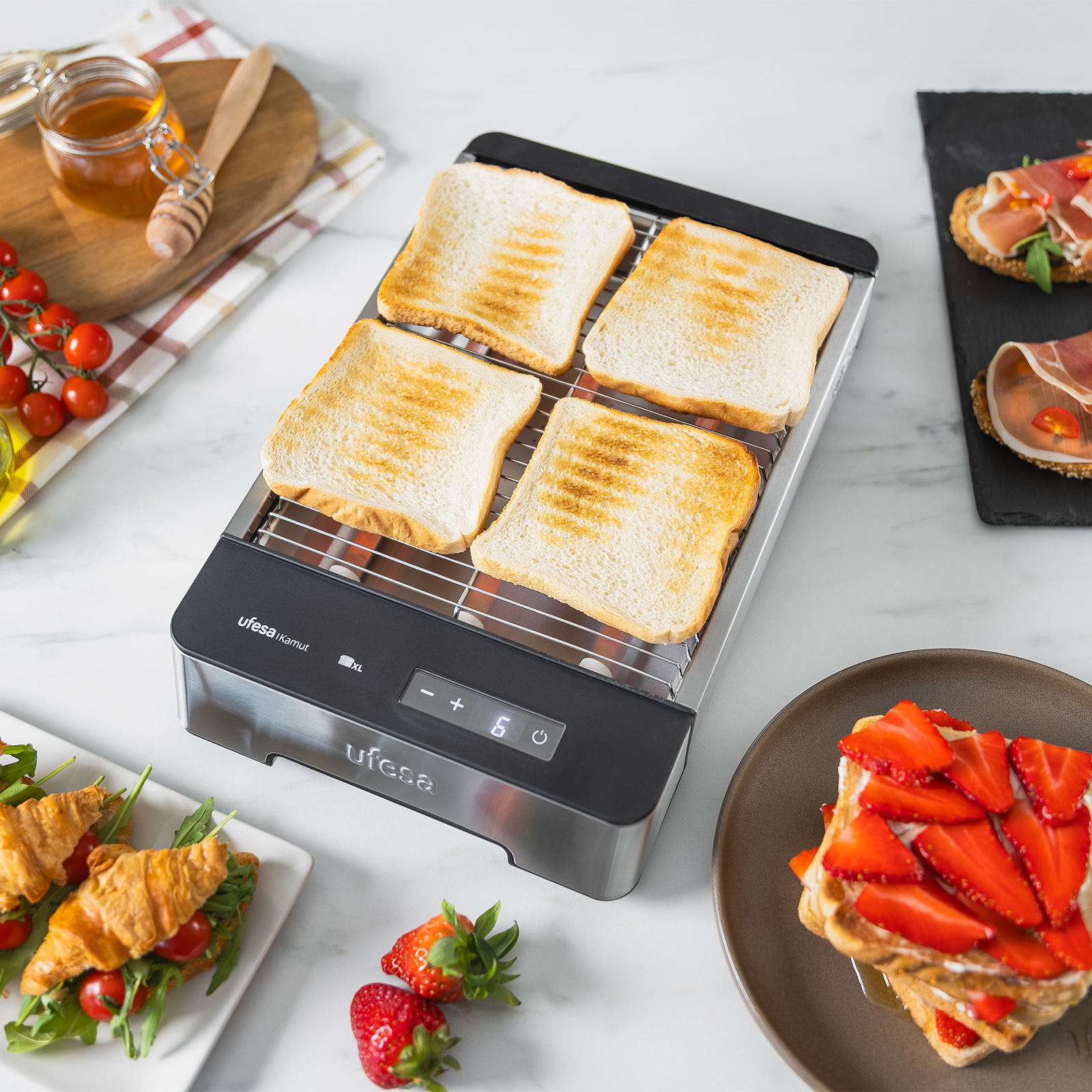 Cuatro rebanadas de pan tostado en una tostadora, con cruasanes, fresas y un tarro de miel.