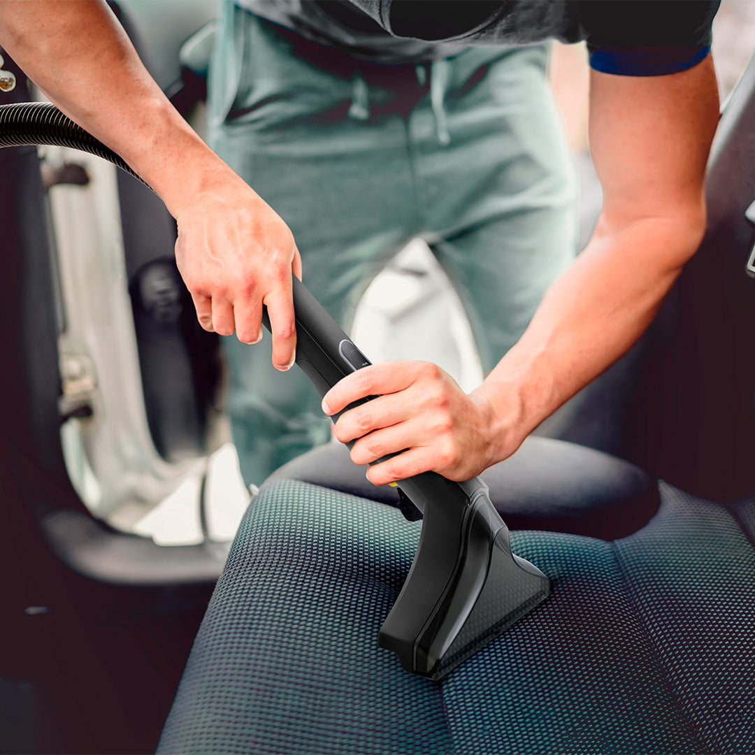 Hombre aspira asiento de coche con accesorio negro.