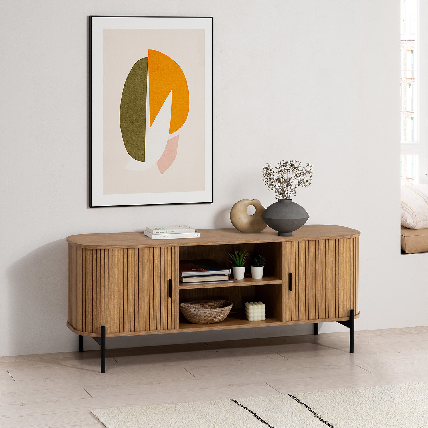 Se muestra un aparador de madera con puertas acanaladas, obras de arte y objetos decorativos.