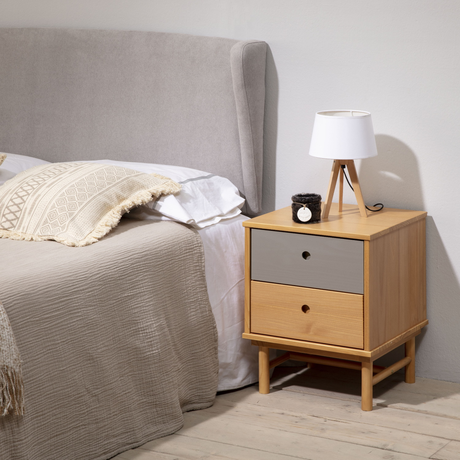 Escena de dormitorio con cama, cabecero gris, mesita de noche de madera con lámpara.