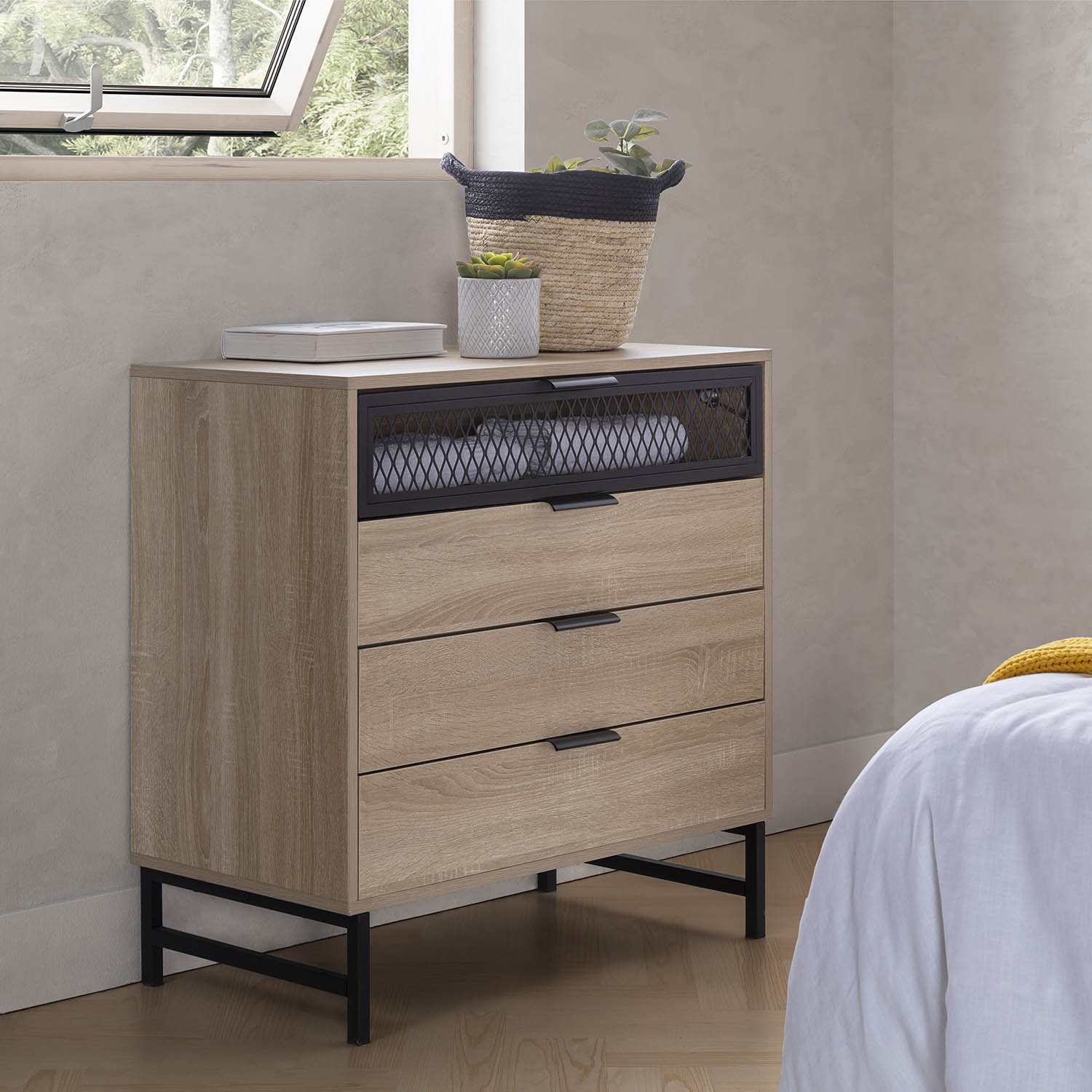 Cómoda de madera con tres cajones y marco de metal negro junto a una cama.