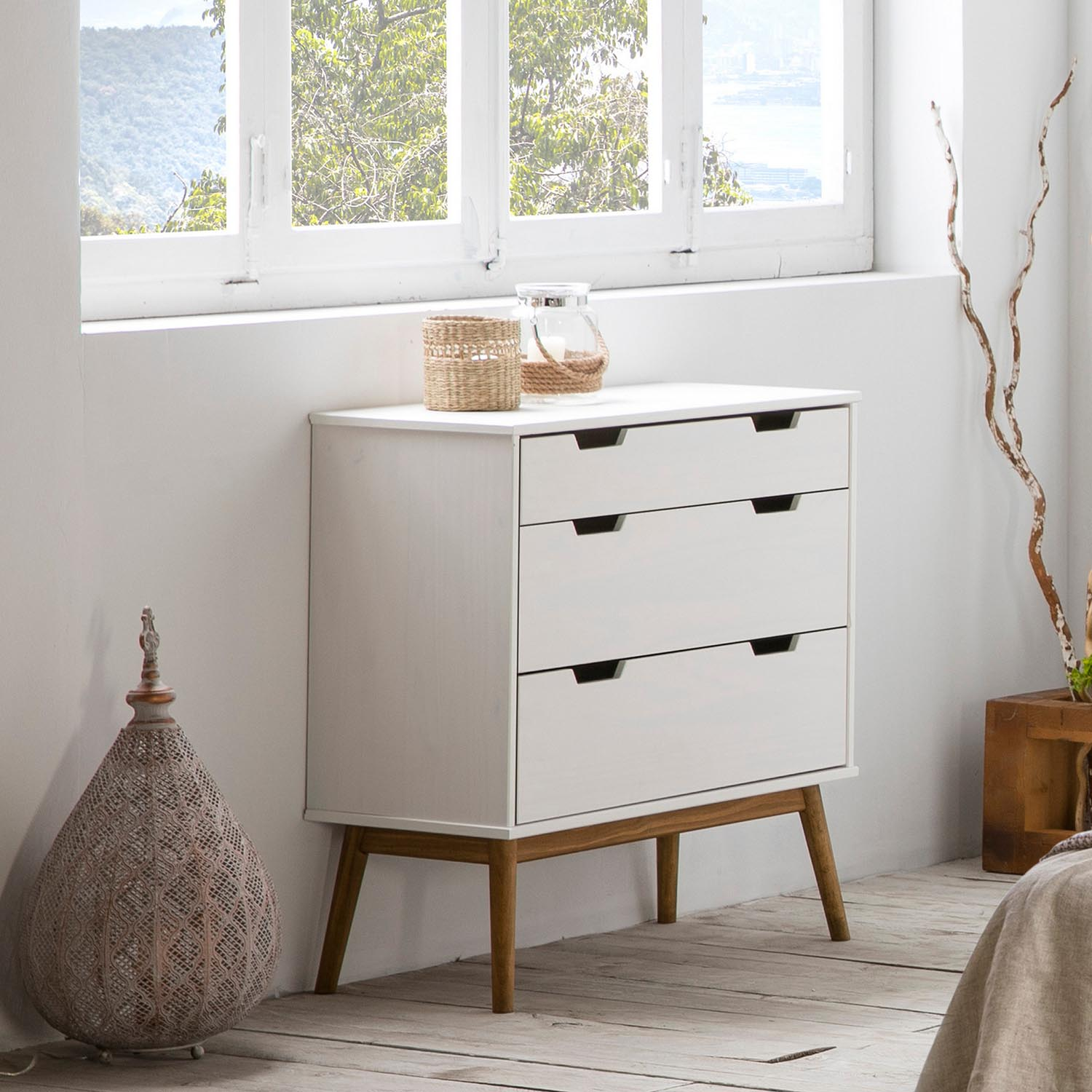 Una cómoda blanca con tres cajones está junto a una ventana.