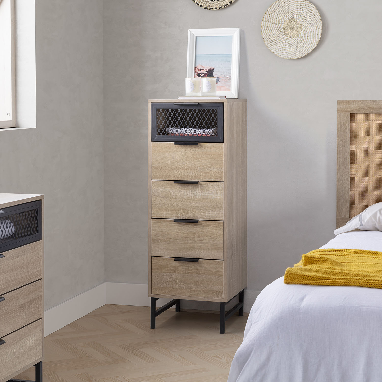 Cómoda de madera con detalles negros junto a una cama con manta amarilla.