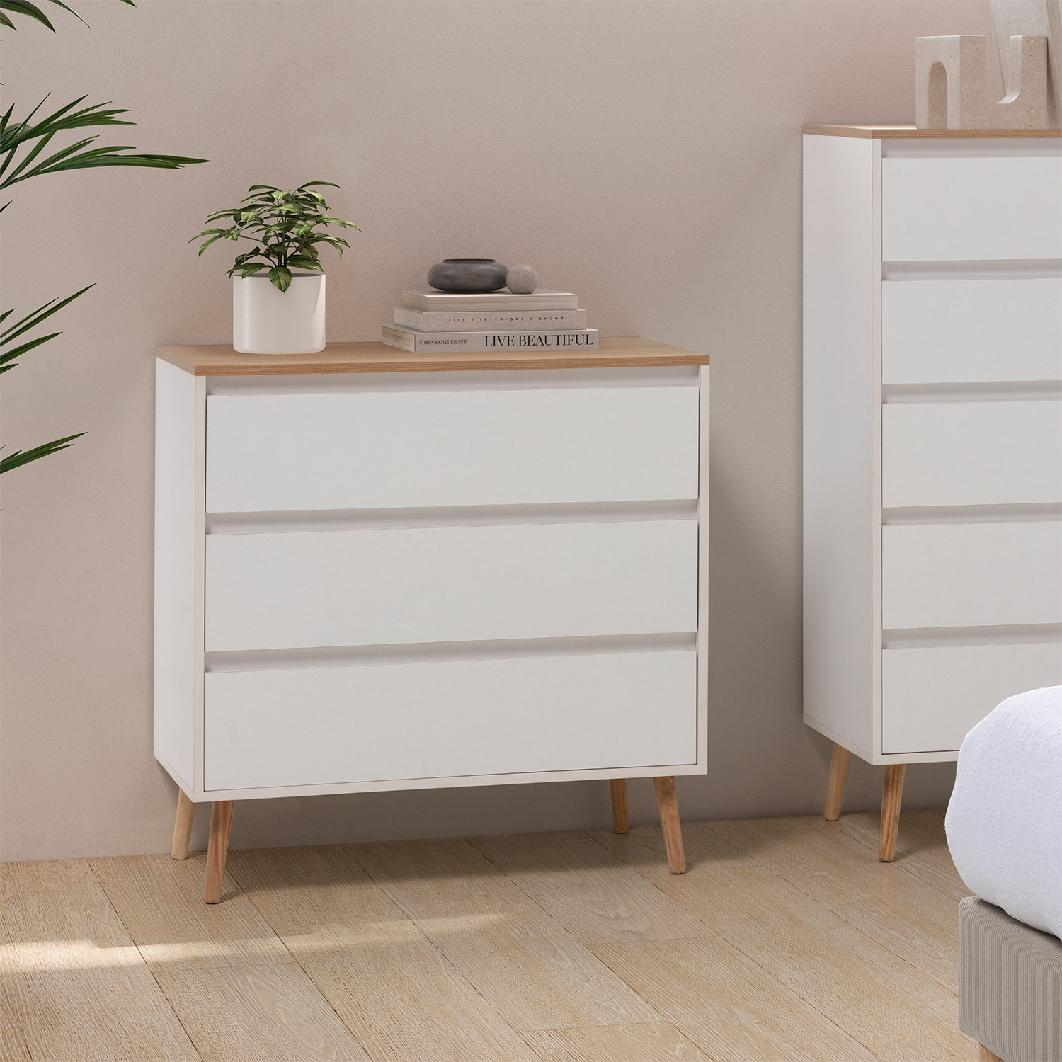 Cómoda blanca con tapa de madera y tres cajones sobre patas.