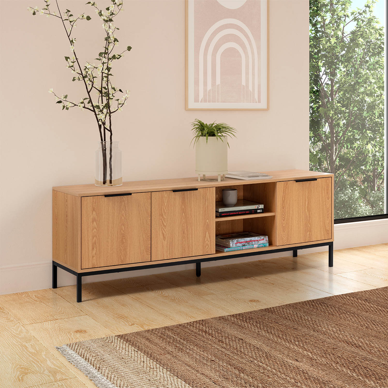 Un mueble de TV de madera clara con patas negras sostiene decoración y libros. Una ventana grande muestra árboles.