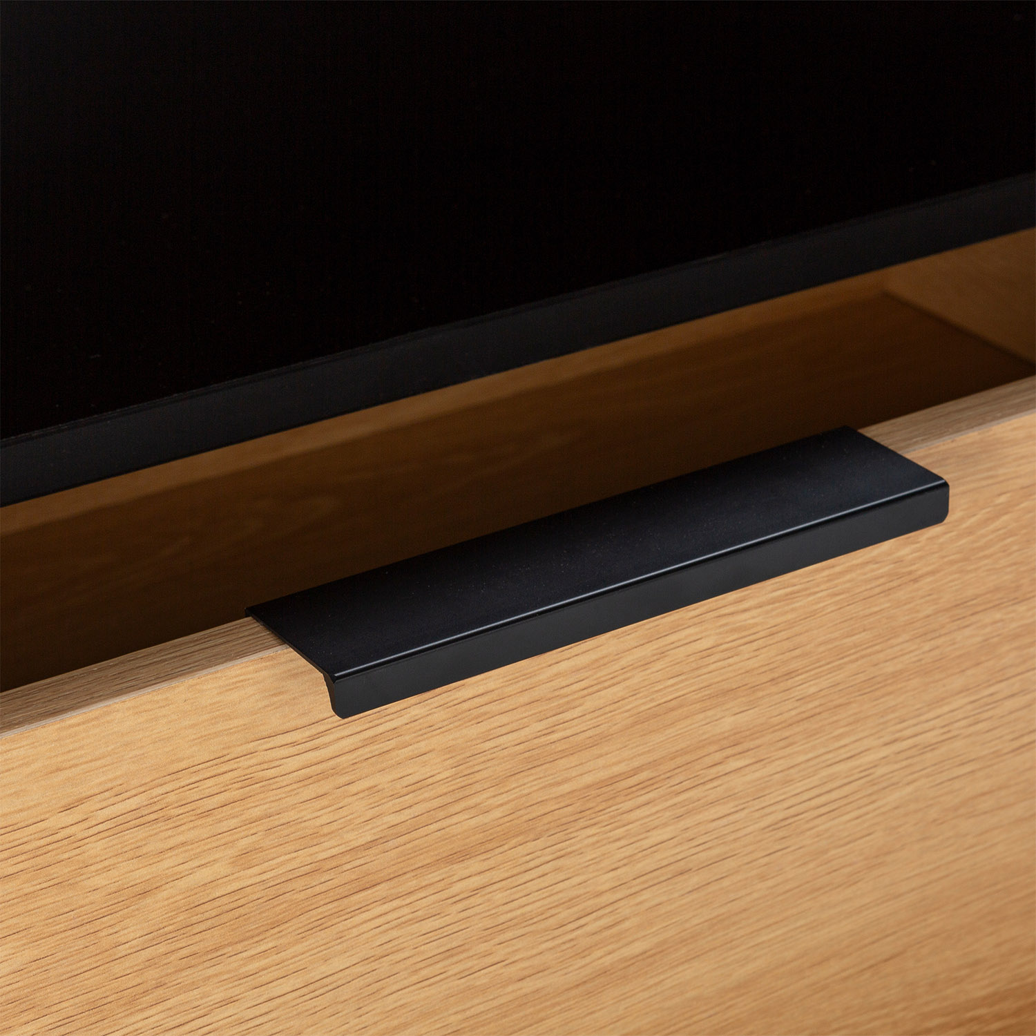 Un cajón de madera abierto con un tirador negro y un interior oscuro.