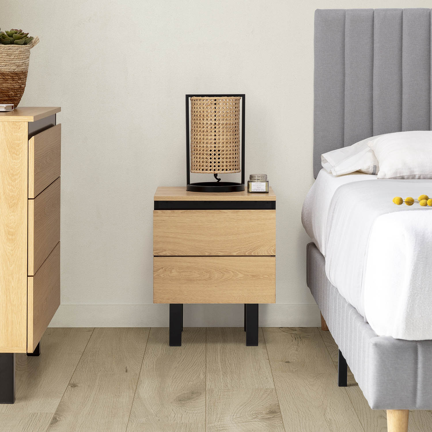 Una mesita de noche de madera con dos cajones junto a una cama con cabecero gris.