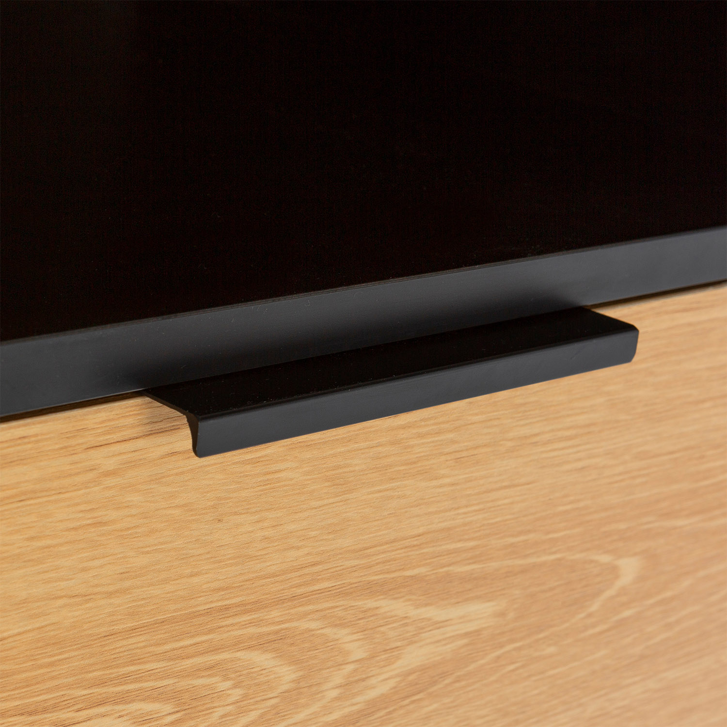 Un tirador negro sobre una superficie de madera con fondo oscuro.