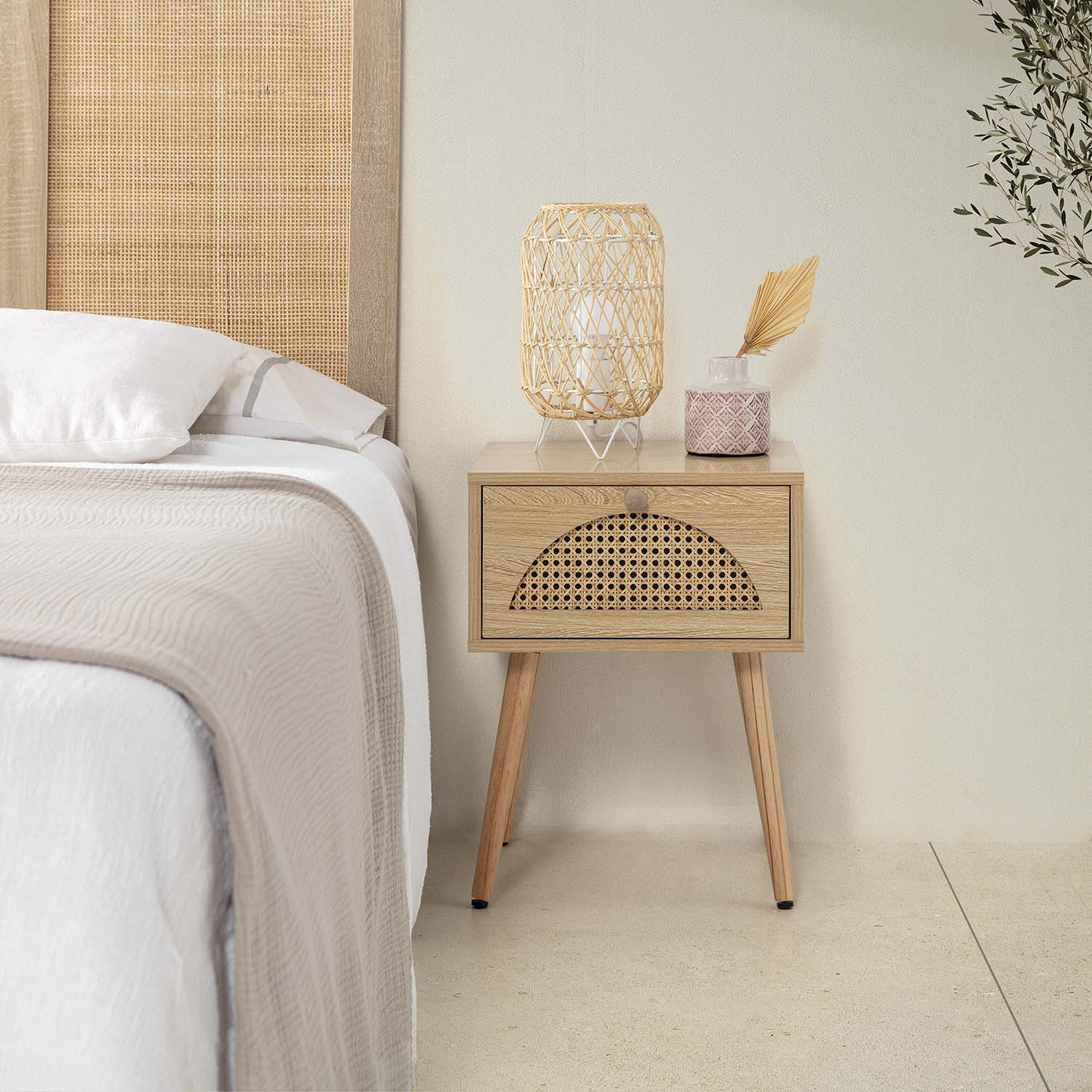 Una mesita de noche de madera con frente de ratán junto a una cama.