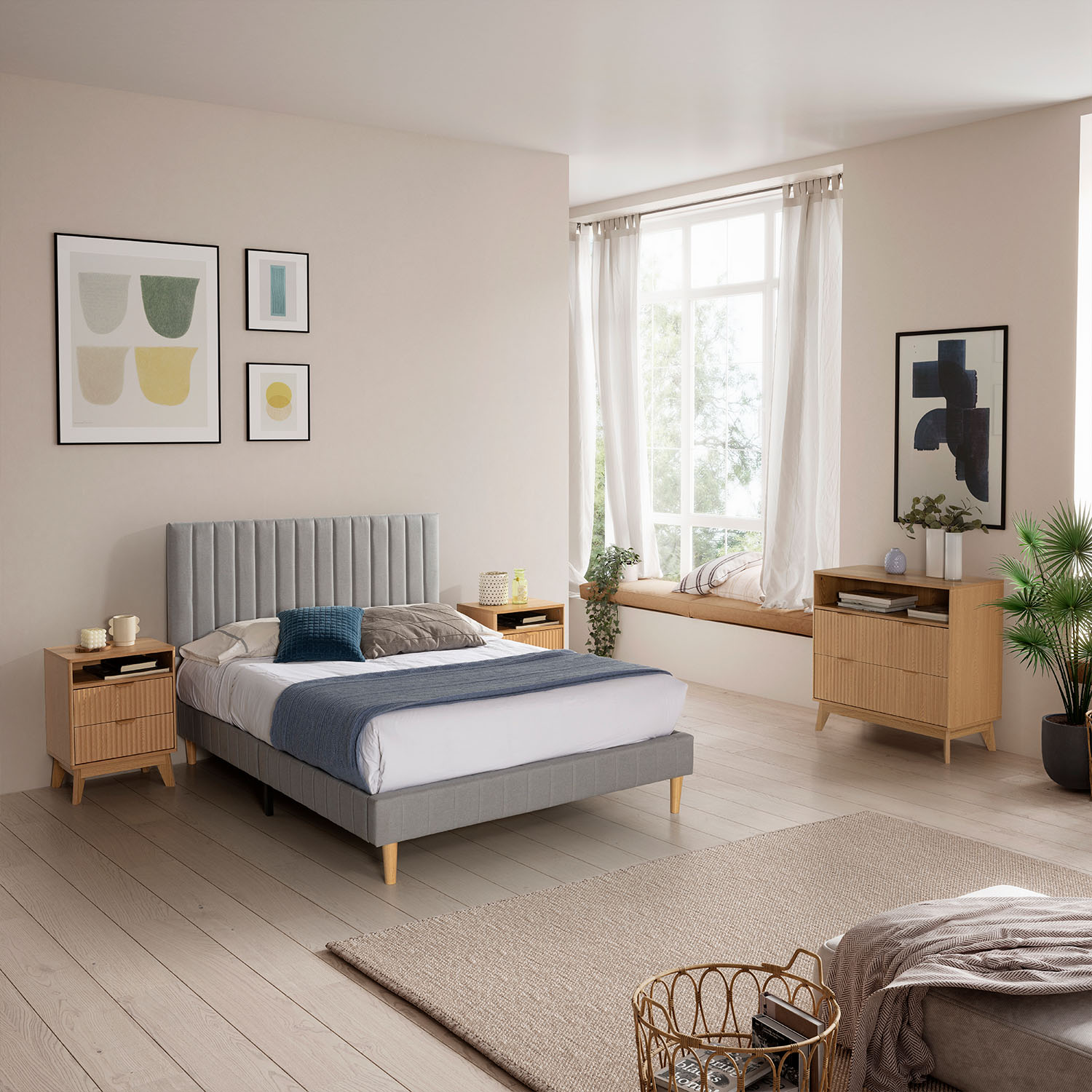 Un dormitorio con cama gris, mesitas de noche de madera y asiento junto a la ventana.