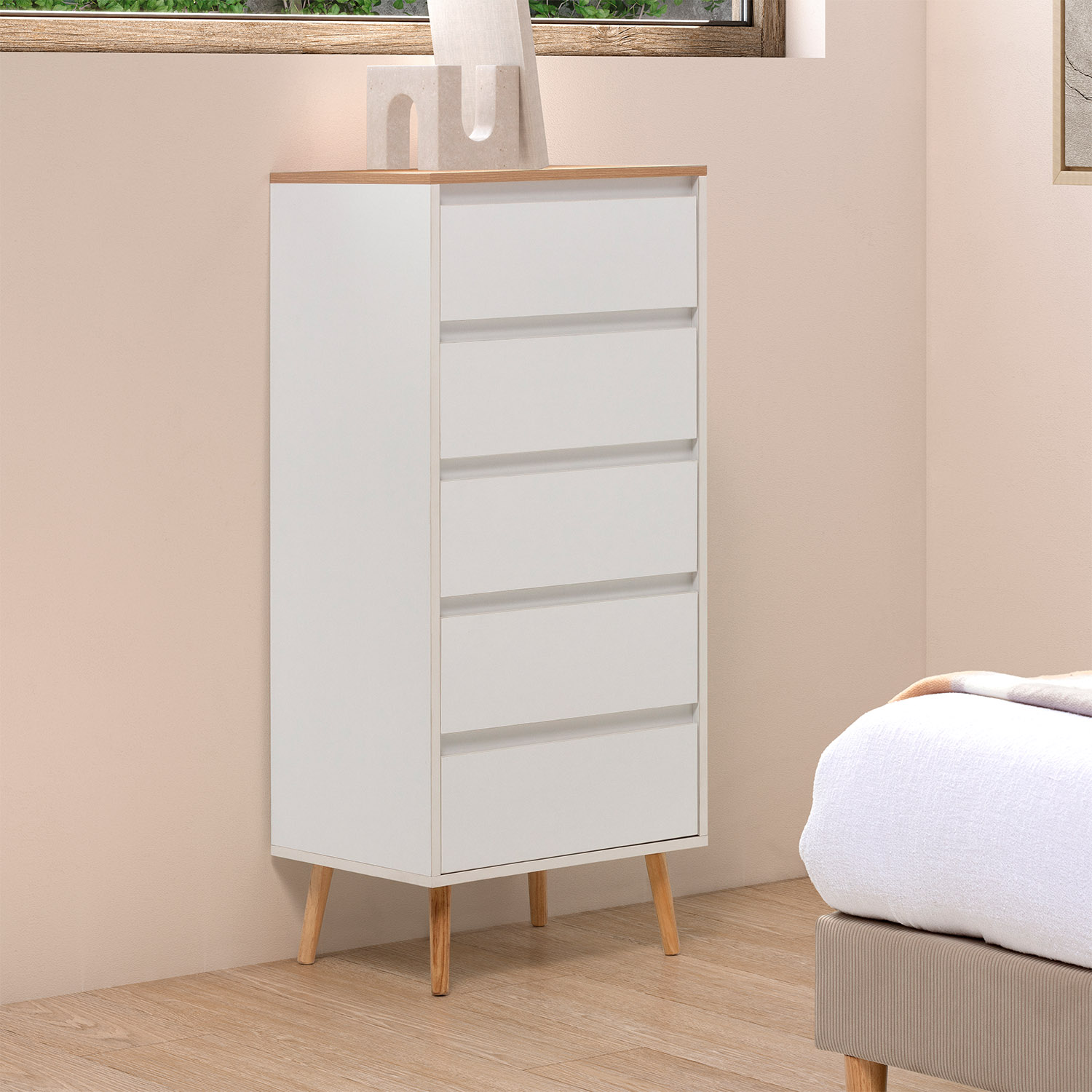 Una cómoda blanca con detalles de madera se apoya en patas de madera junto a una cama.